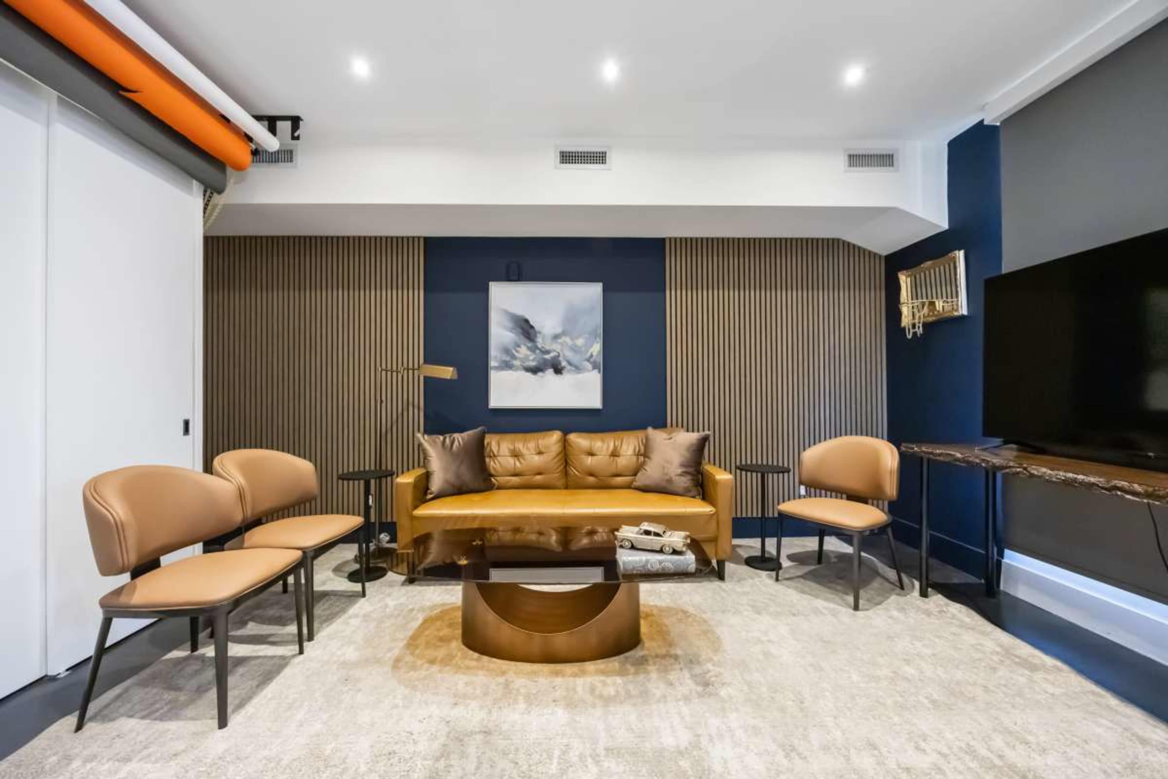 The image features a modern living room with a brown leather sofa, four matching chairs, a glass coffee table, and a large TV mounted on the wall.