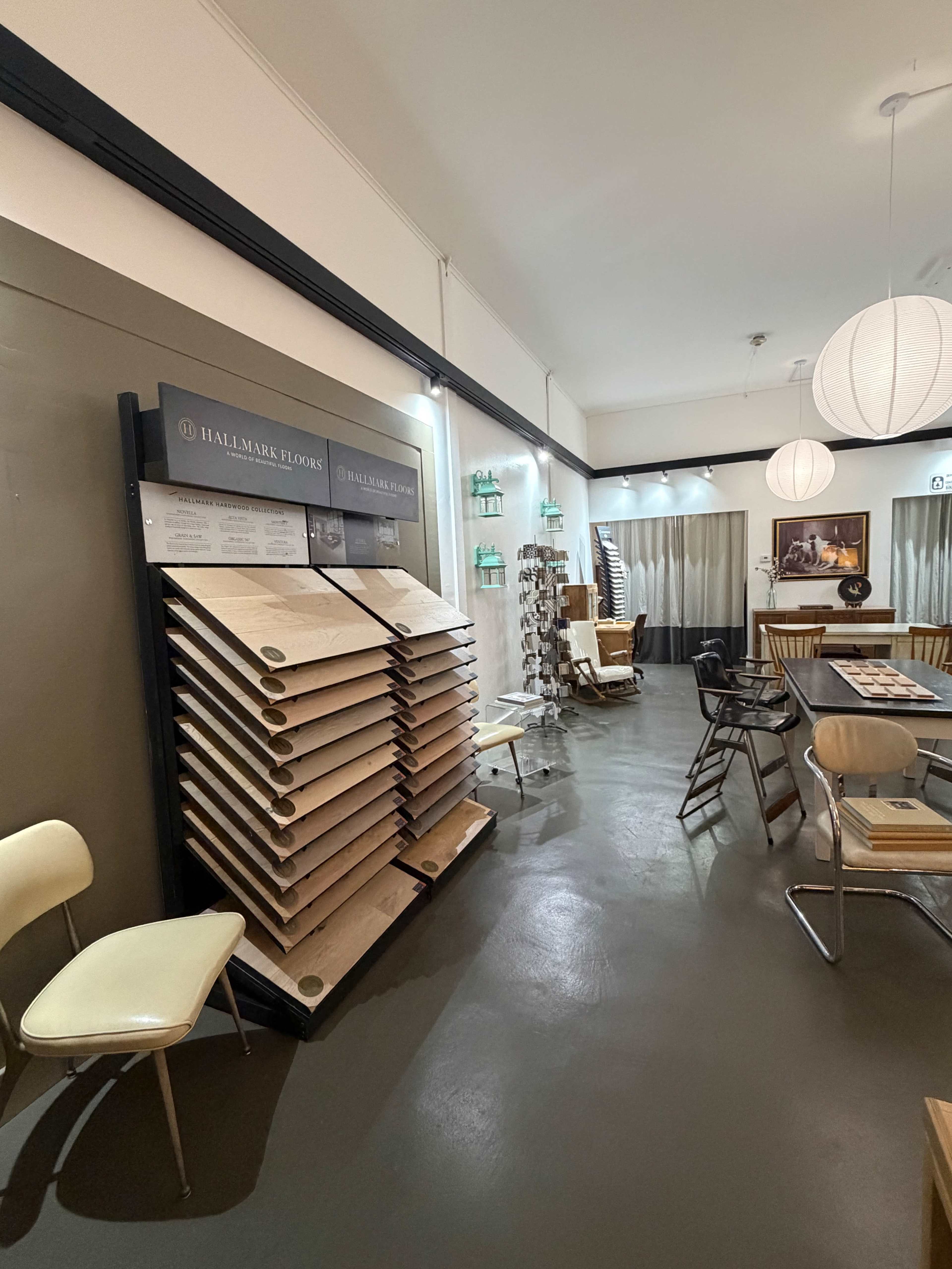 The image shows a sample display of hardwood flooring next to seating and decorative items in a well-lit interior space.