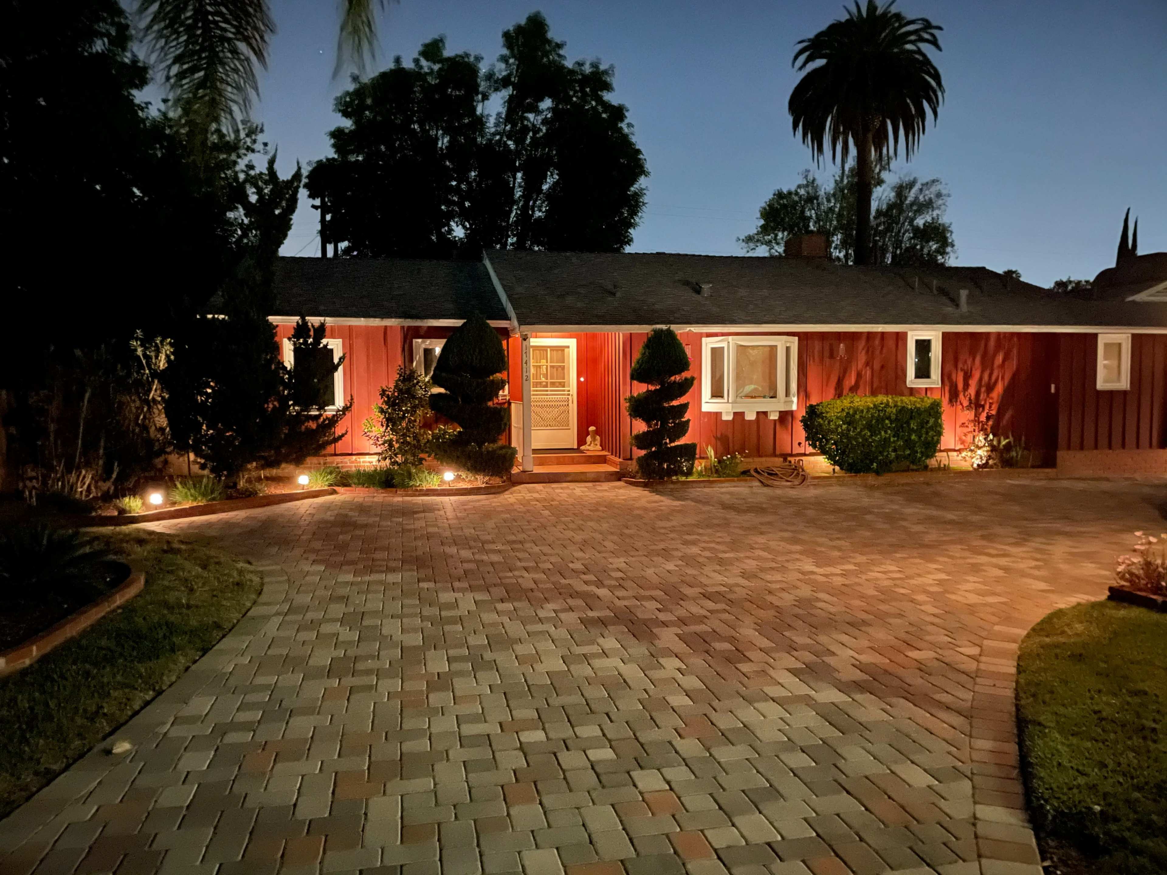 A red house with a path of paved stones is illuminated by landscape lights at dusk.