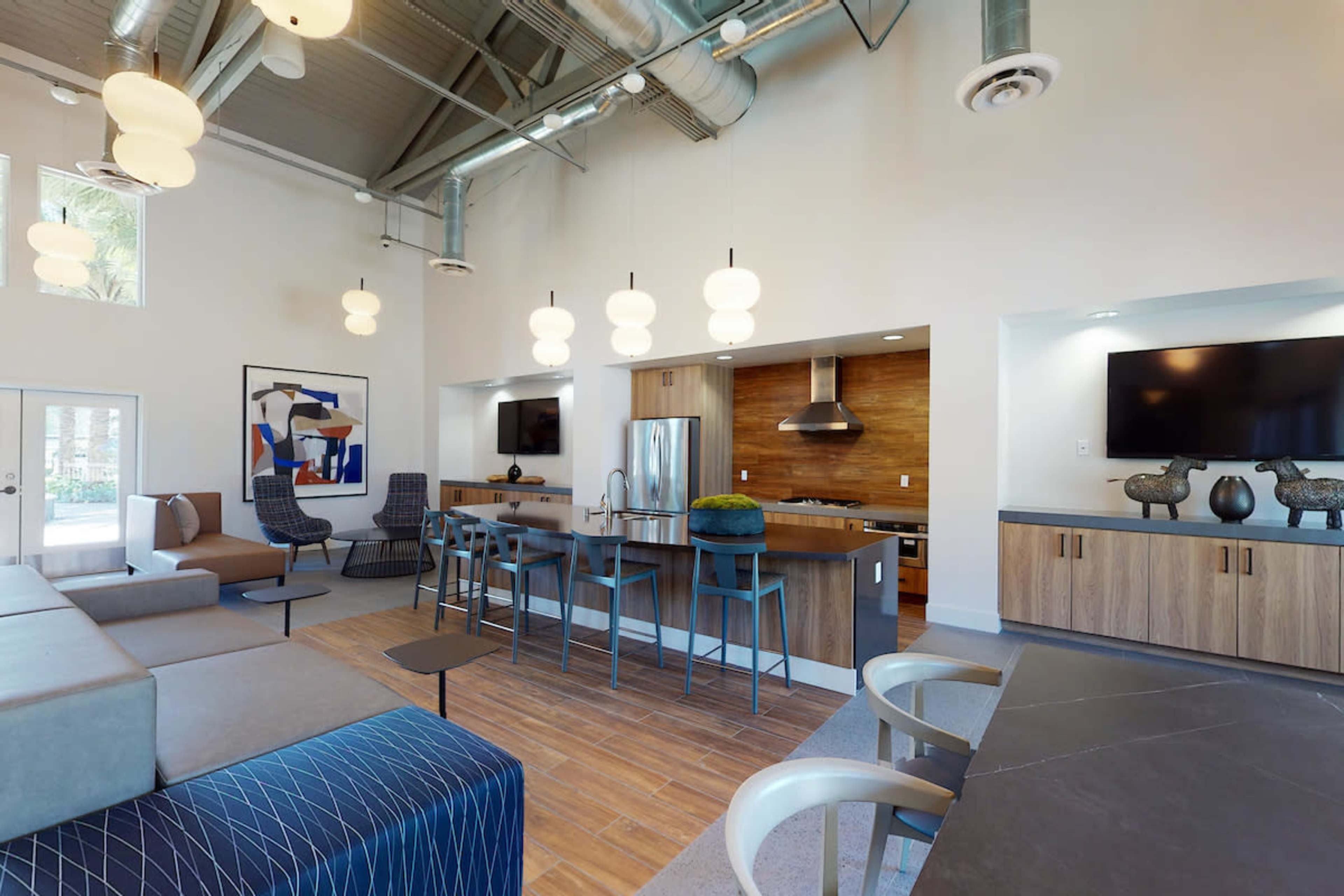 A modern common area with seating, a kitchen, and dining space featuring pendant lighting and wooden accents.