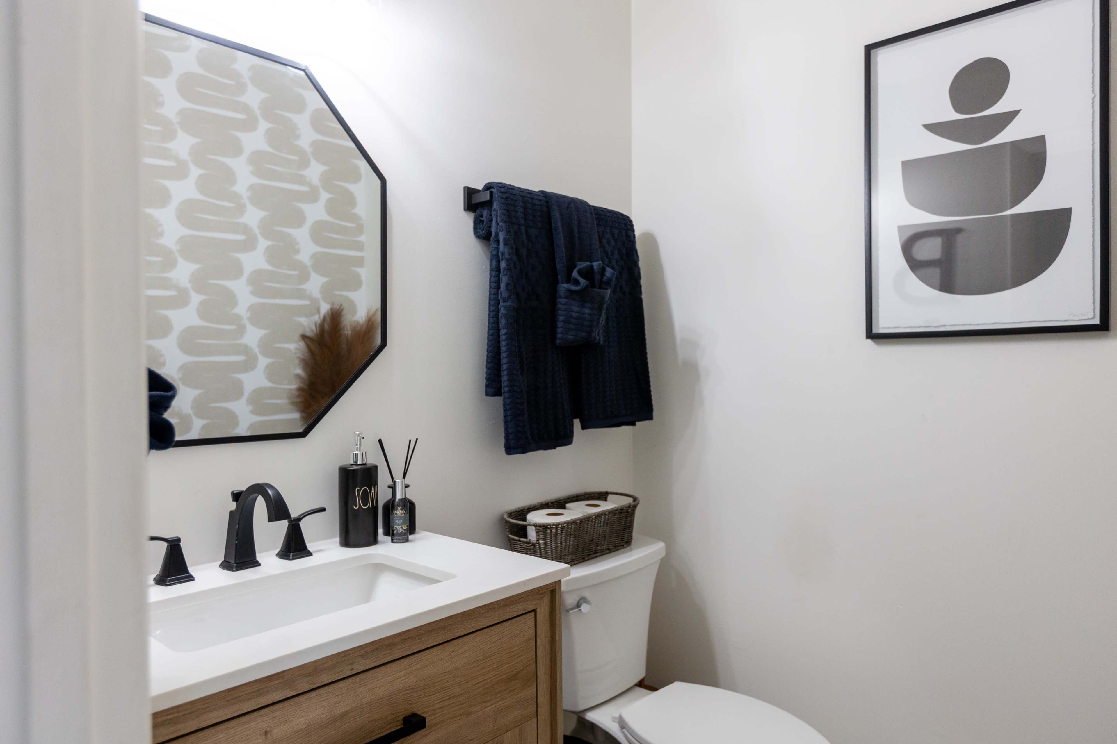 A small bathroom featuring a vanity with a mirror, a toilet, and decorative items on the counter, along with a framed abstract art piece on the wall.