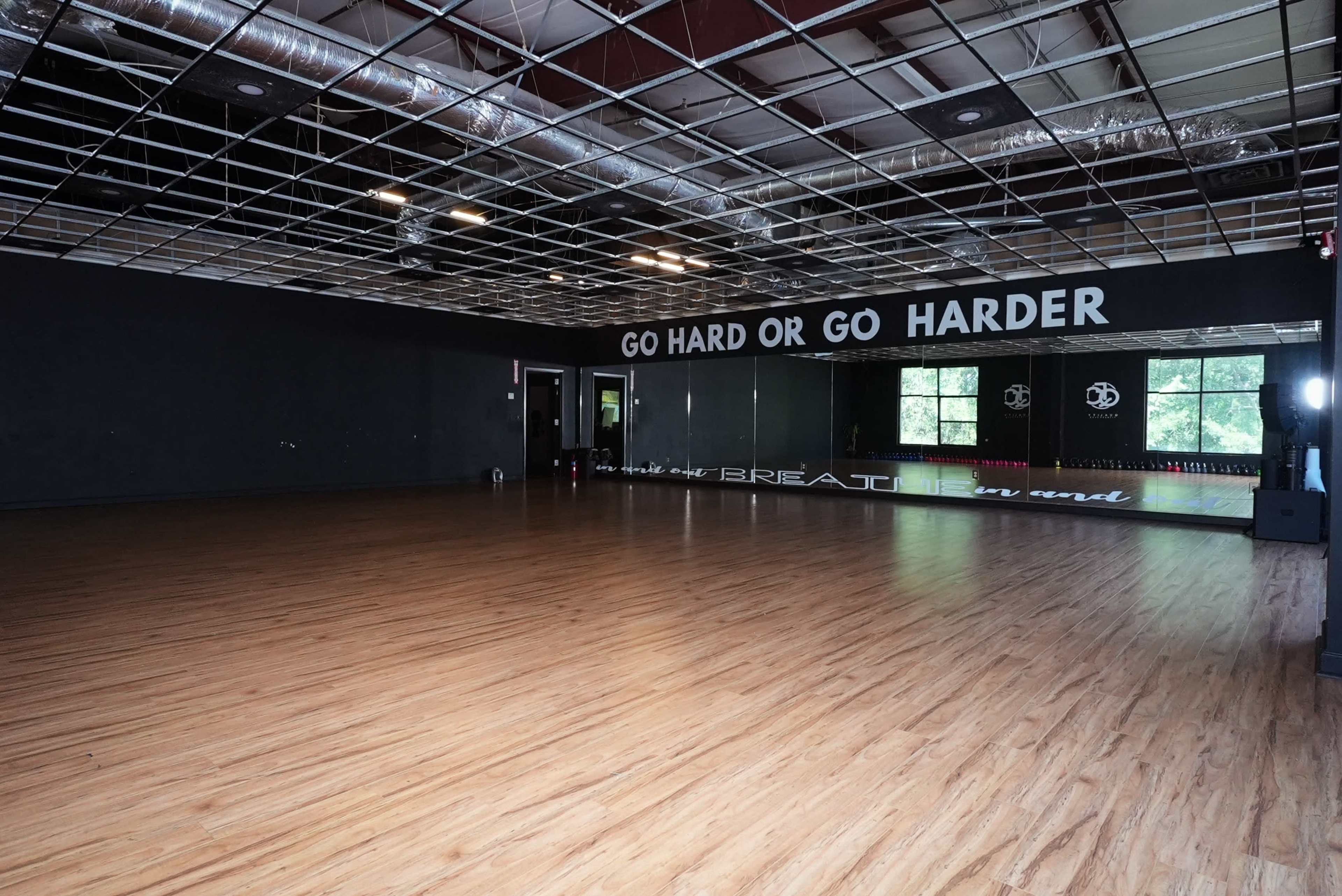 The image shows a spacious dance studio with a wooden floor and large mirrors, featuring motivational text on the walls.