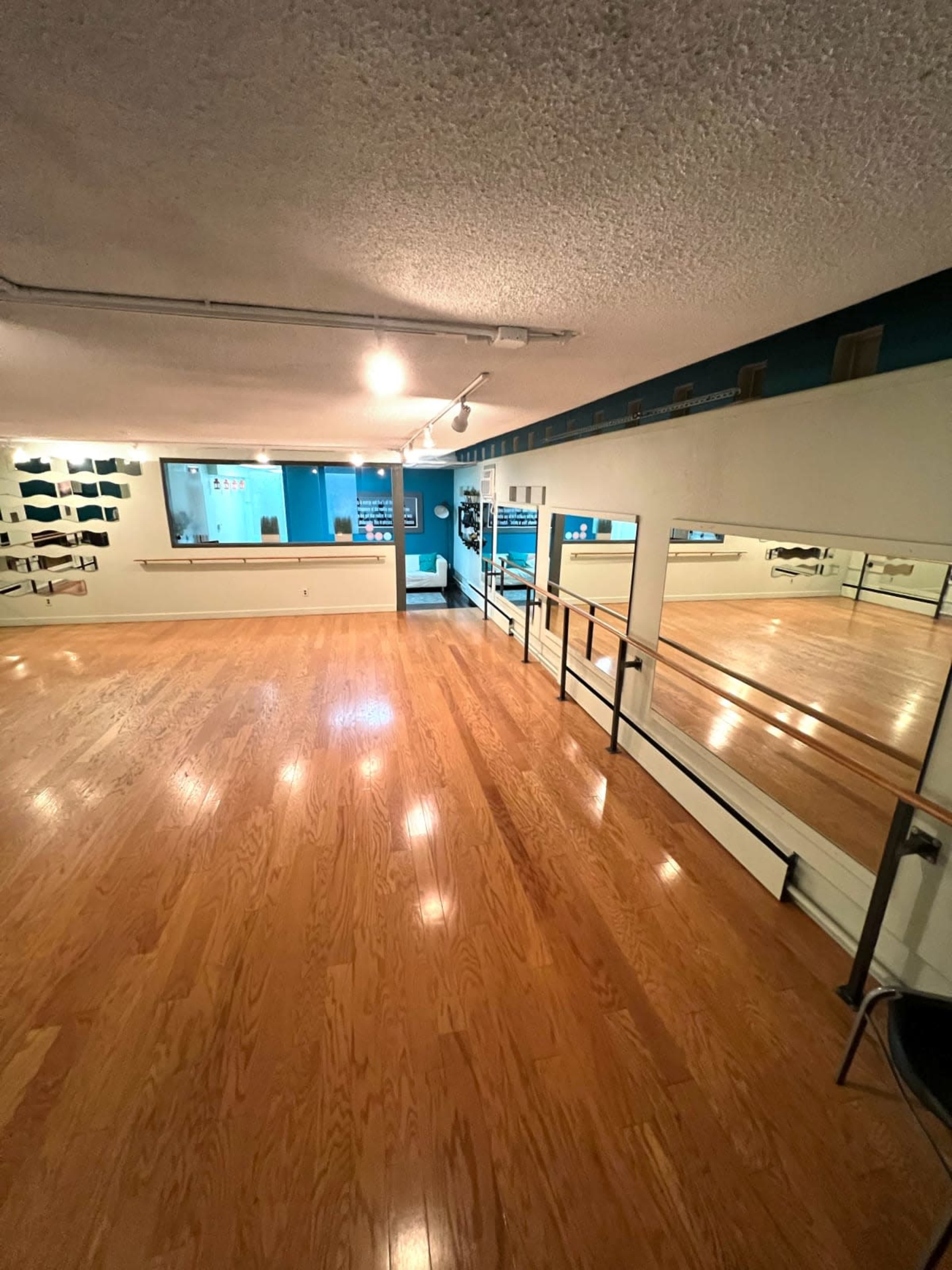 The image shows a spacious dance studio with wooden flooring, mirrors on one wall, and a bright blue accent wall in the background.