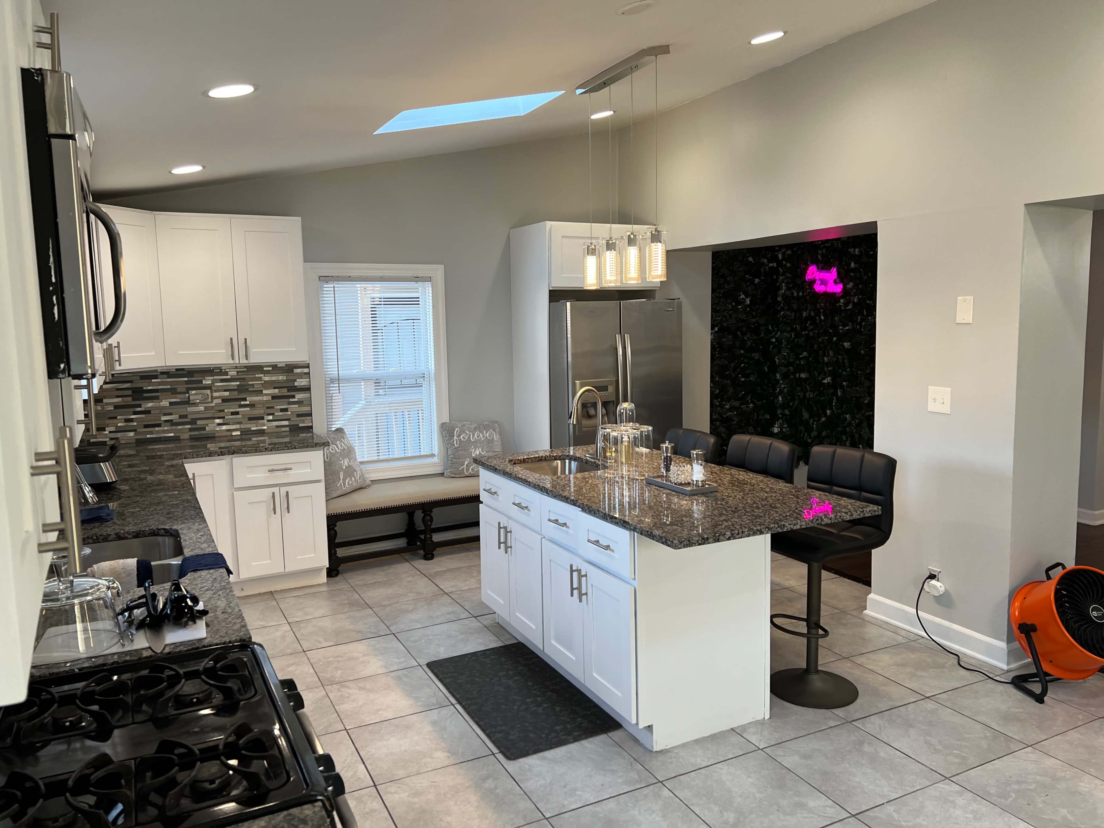 A modern kitchen features white cabinetry, a large island with seating, and a dining nook by the window.
