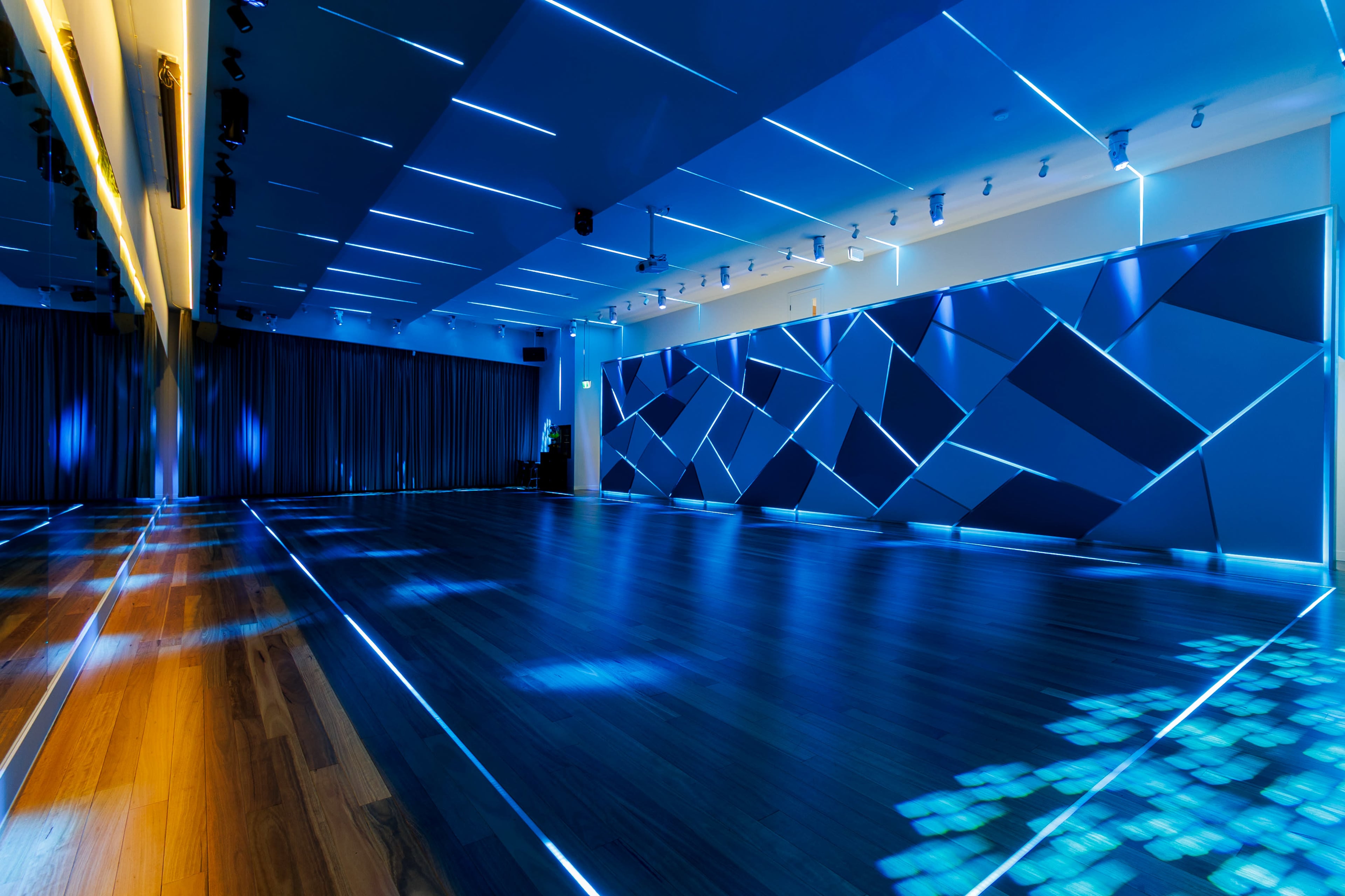 The image shows a spacious room with wooden flooring, illuminated by blue LED lights that create geometric patterns on the walls and floor.