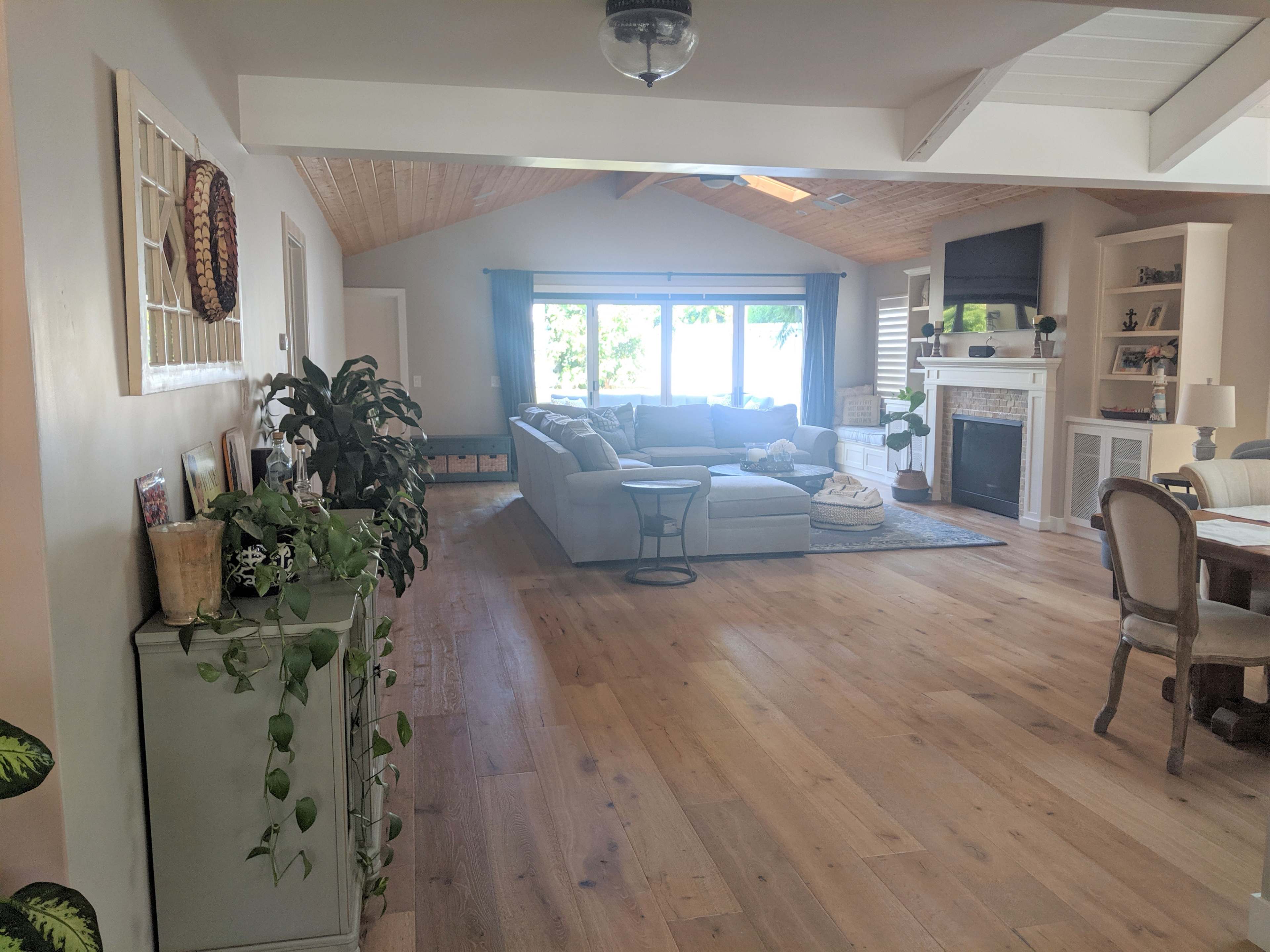 The room features a spacious living area with a large sectional sofa, a coffee table, and a dining area, all illuminated by natural light from large windows.