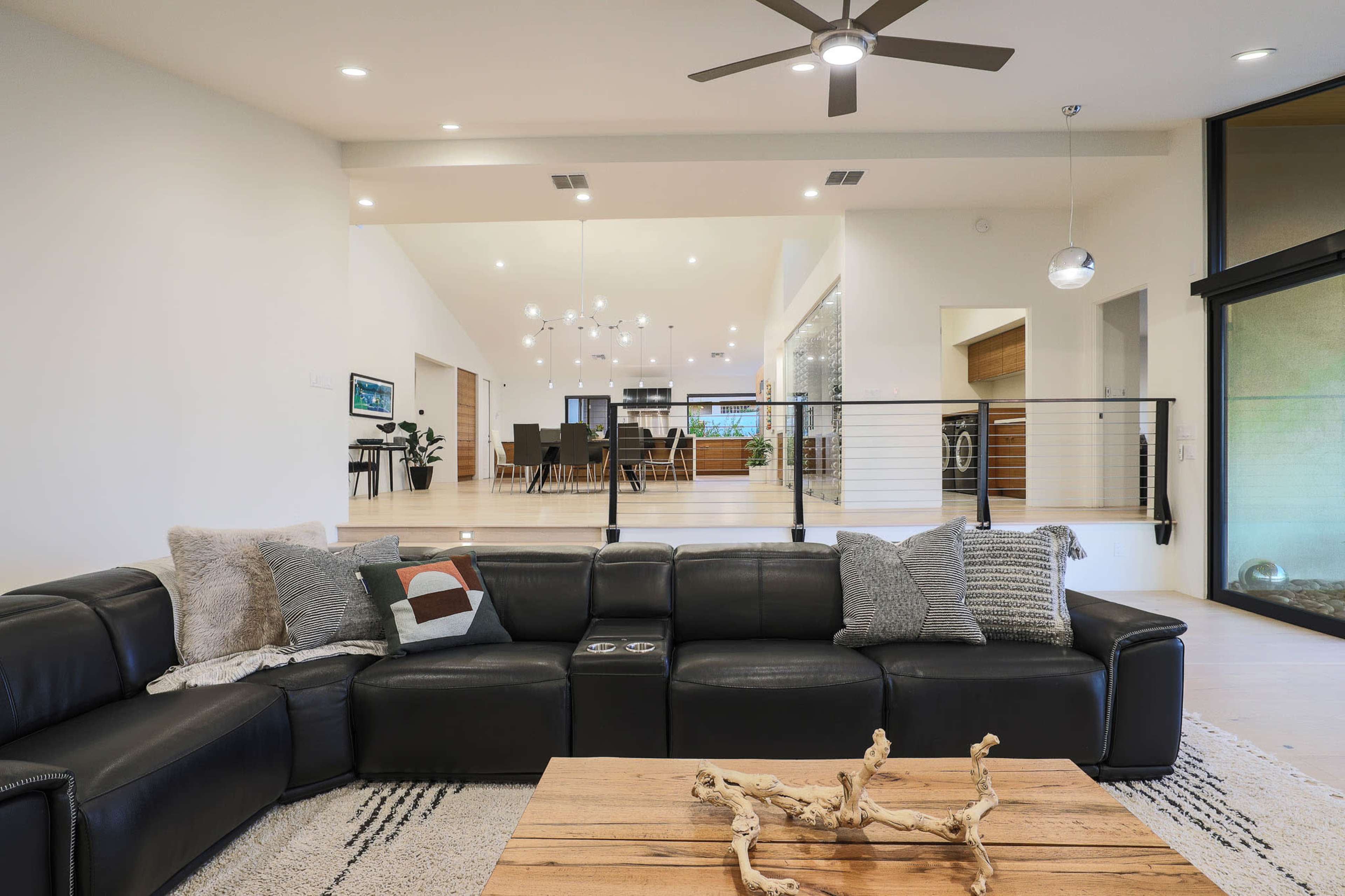 A modern living room featuring a black sectional sofa, a wooden coffee table with decorative accents, and an open layout that connects to a dining area in the background.