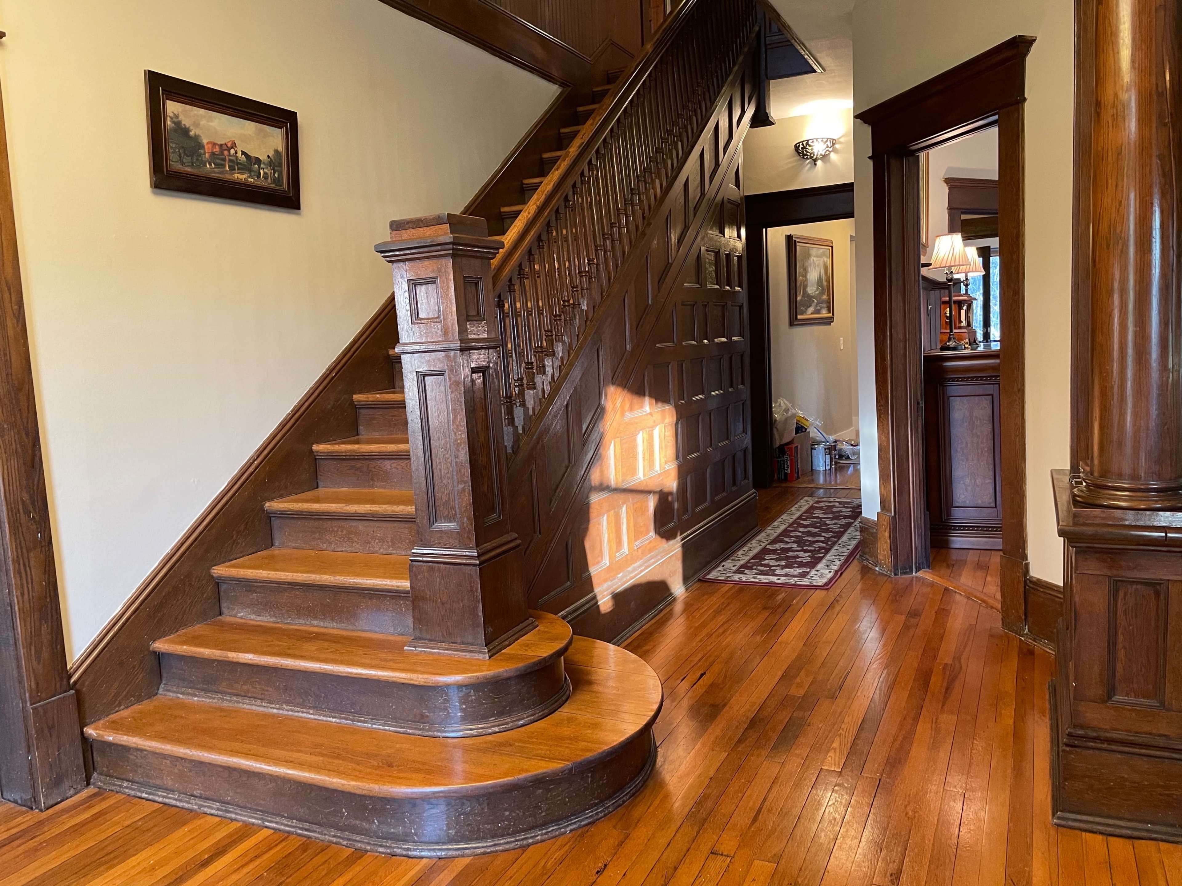 A wooden staircase with a curved landing leads up from a spacious hallway featuring polished hardwood floors and ornate woodwork.