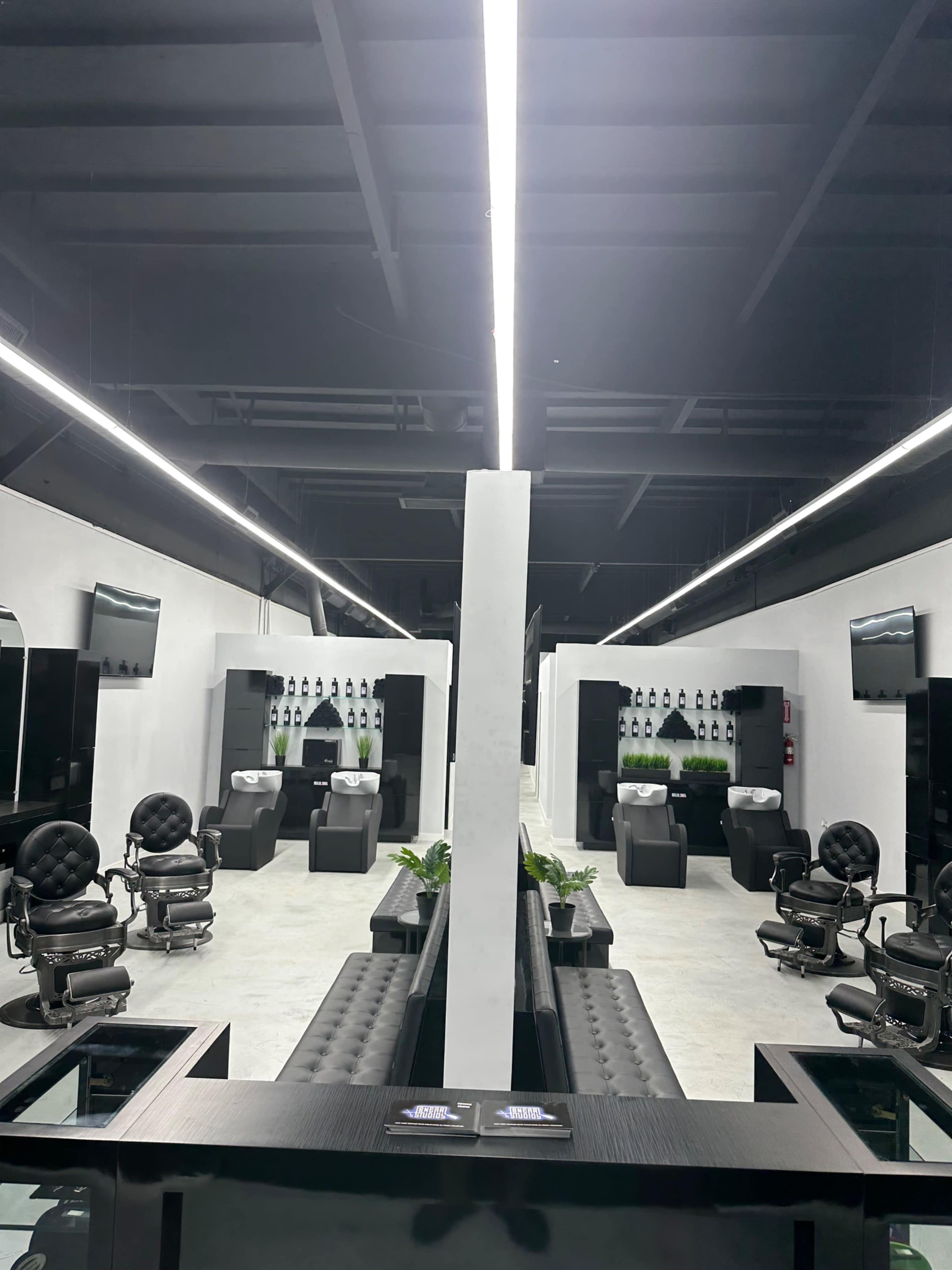 The image shows a modern hair salon with black styling chairs, wash stations, and overhead lighting in a spacious layout.