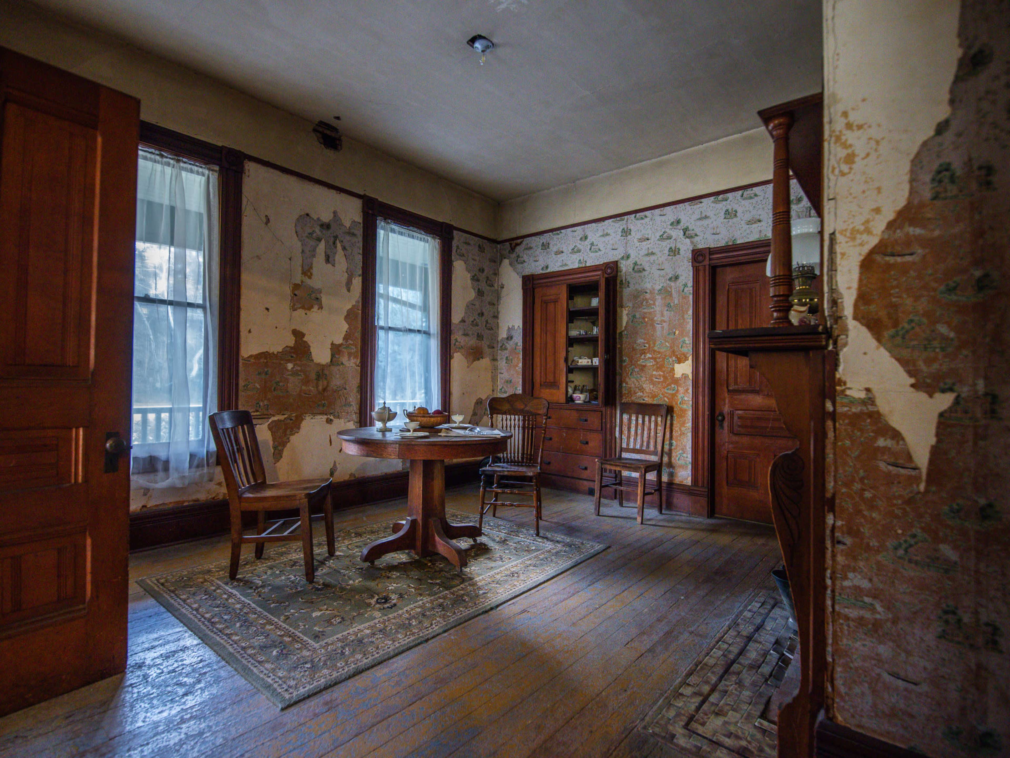 A vintage interior room with a round wooden table, four chairs, and peeling wallpaper.