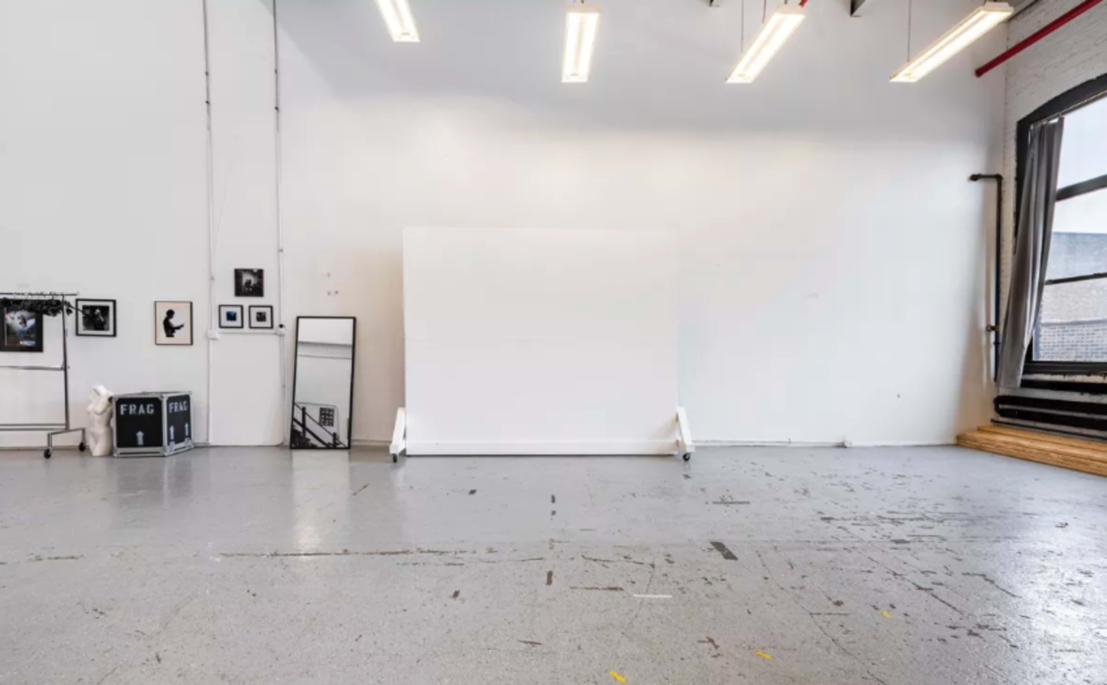 A spacious, minimalist studio with a large white backdrop, framed photographs on the walls, and a window letting in natural light.