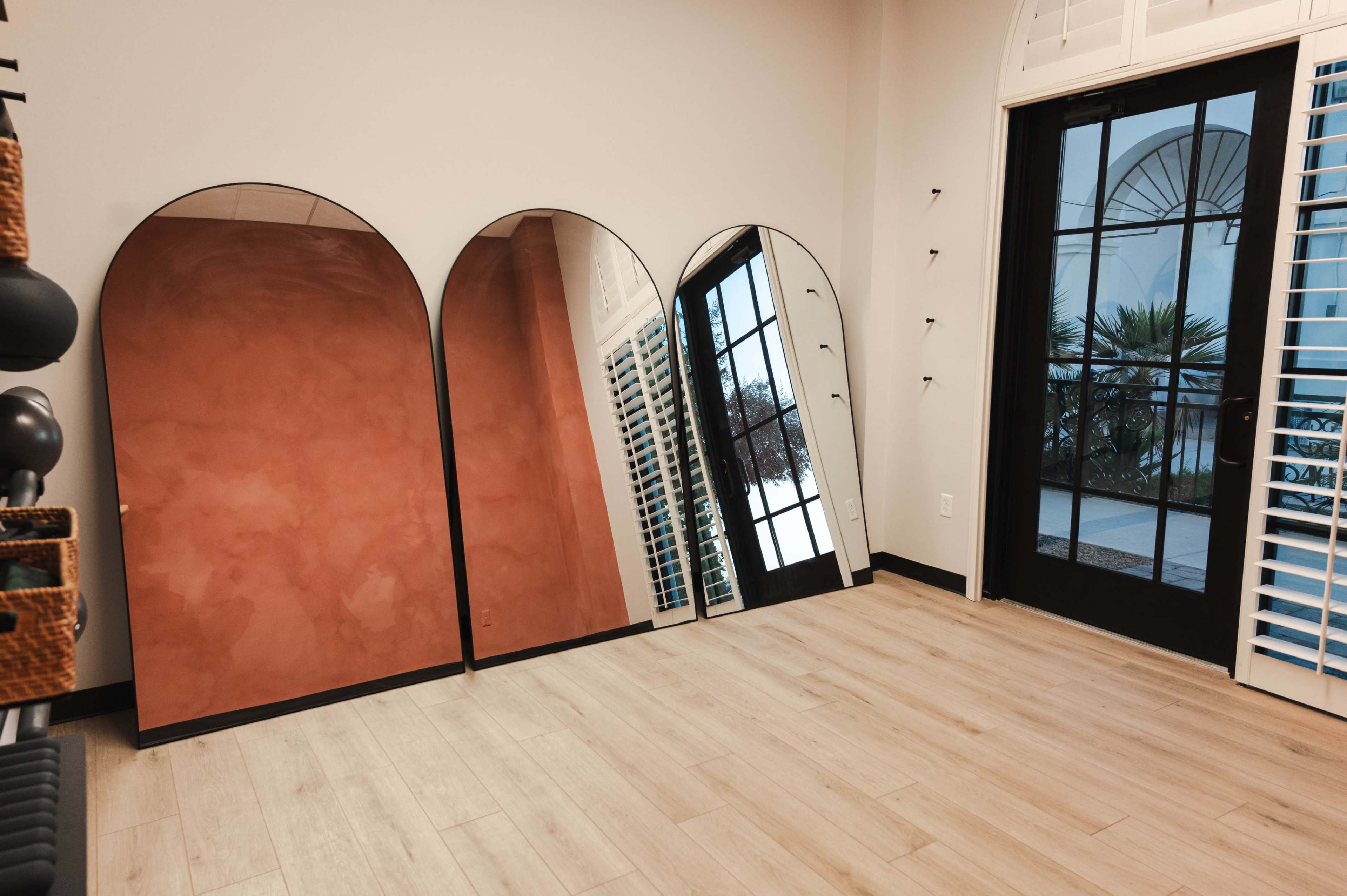 The image shows three arched mirrors reflecting a room with wooden flooring and a doorway leading outside.