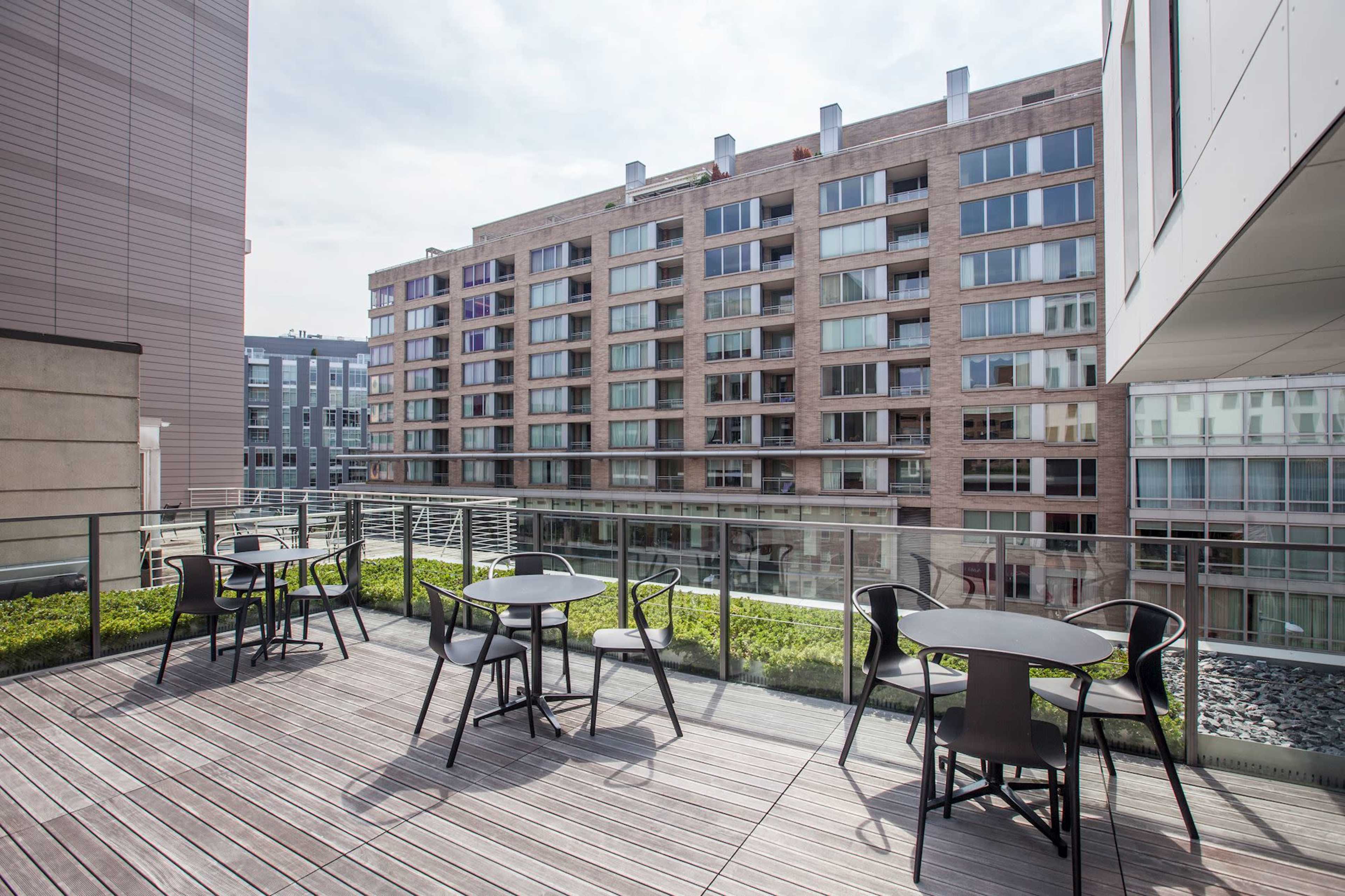 The image shows a balcony area with several black tables and chairs overlooking a row of modern apartment buildings.