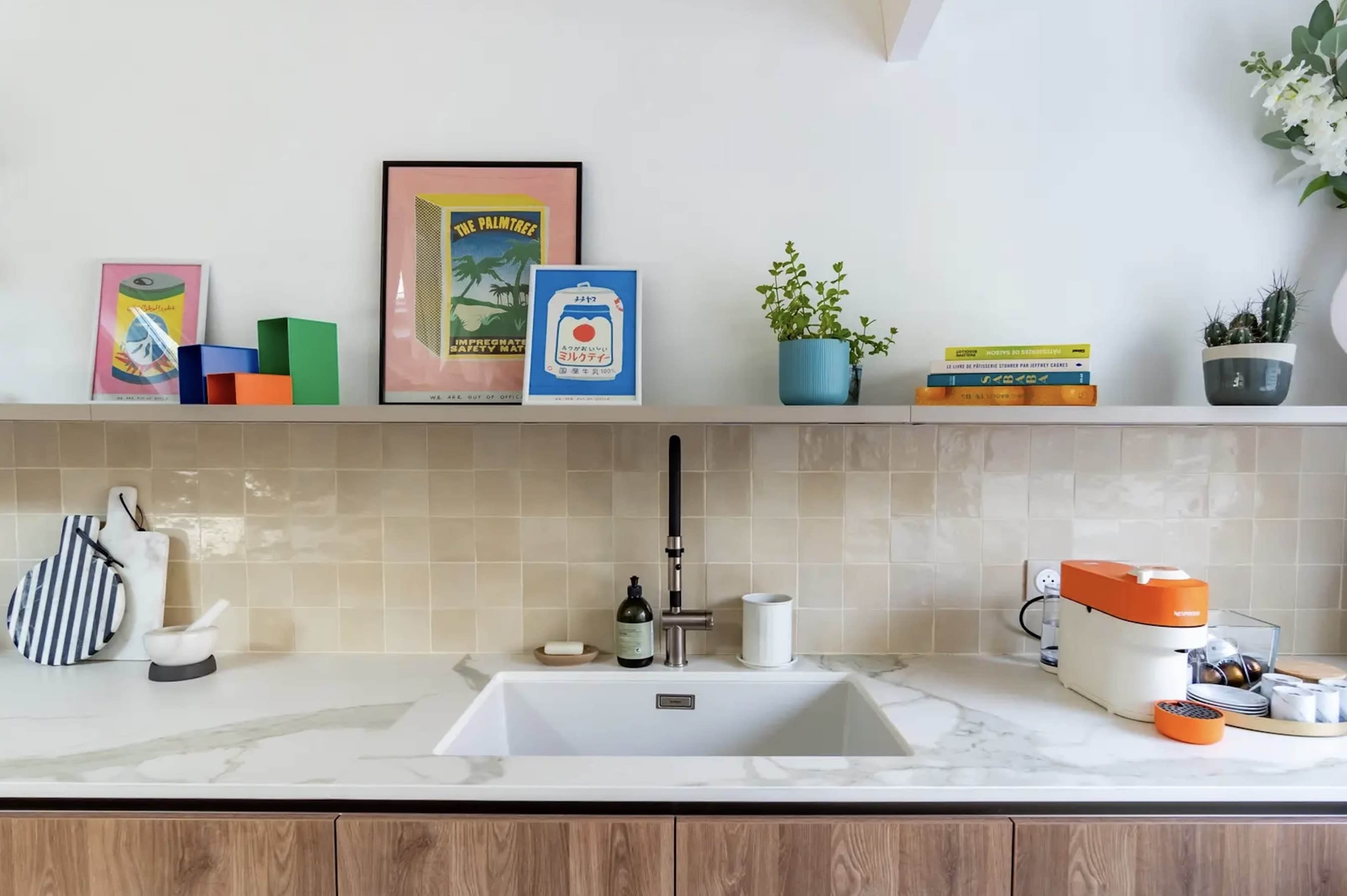 The image shows a modern kitchen countertop with a large sink, various colorful decorative items on a shelf above, and a few kitchen appliances.