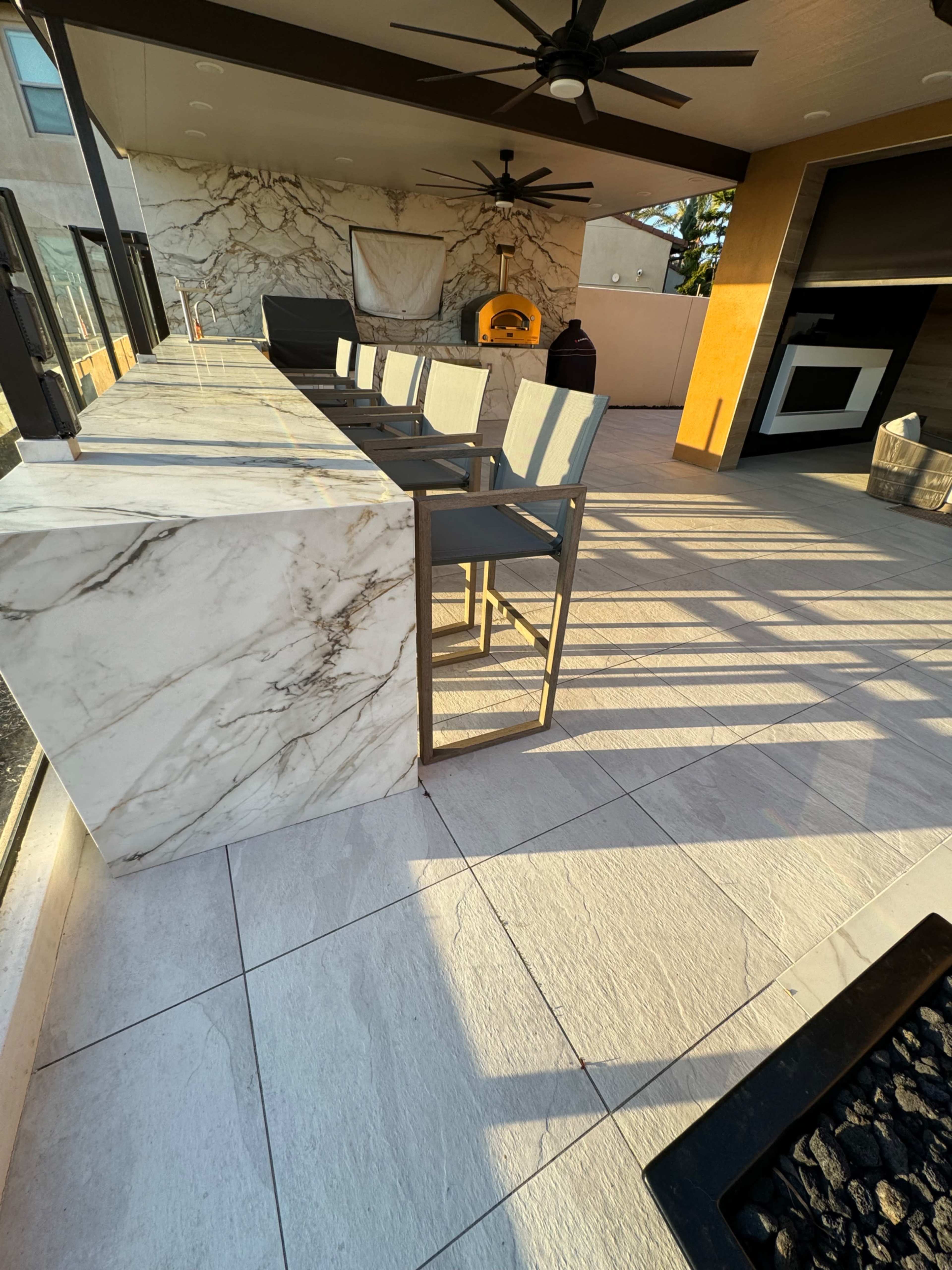A spacious outdoor area with a marble-topped bar and several gray chairs, featuring a modern design and a wall with a textured finish.