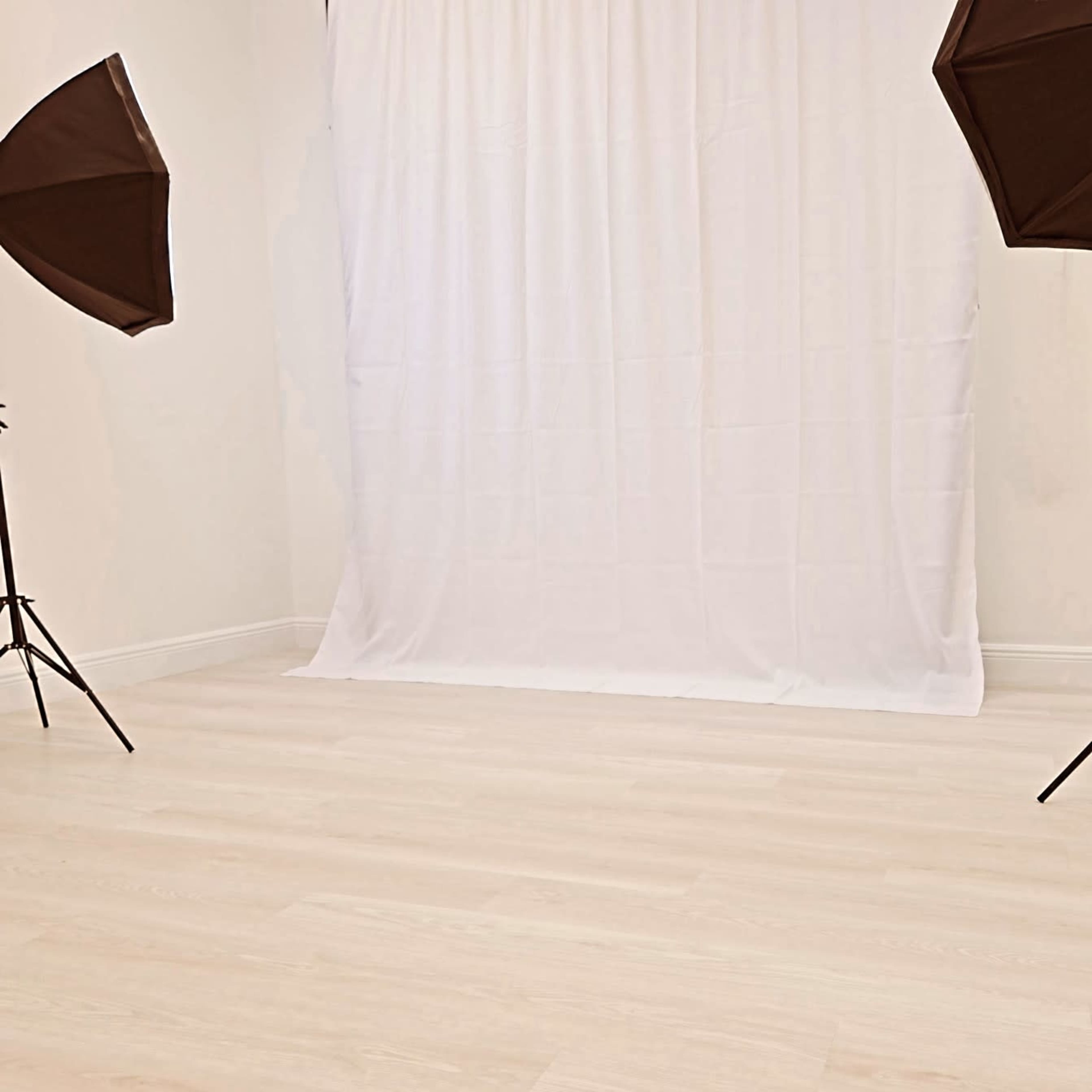 An empty photography studio with a white backdrop and two lighting stands positioned on either side.