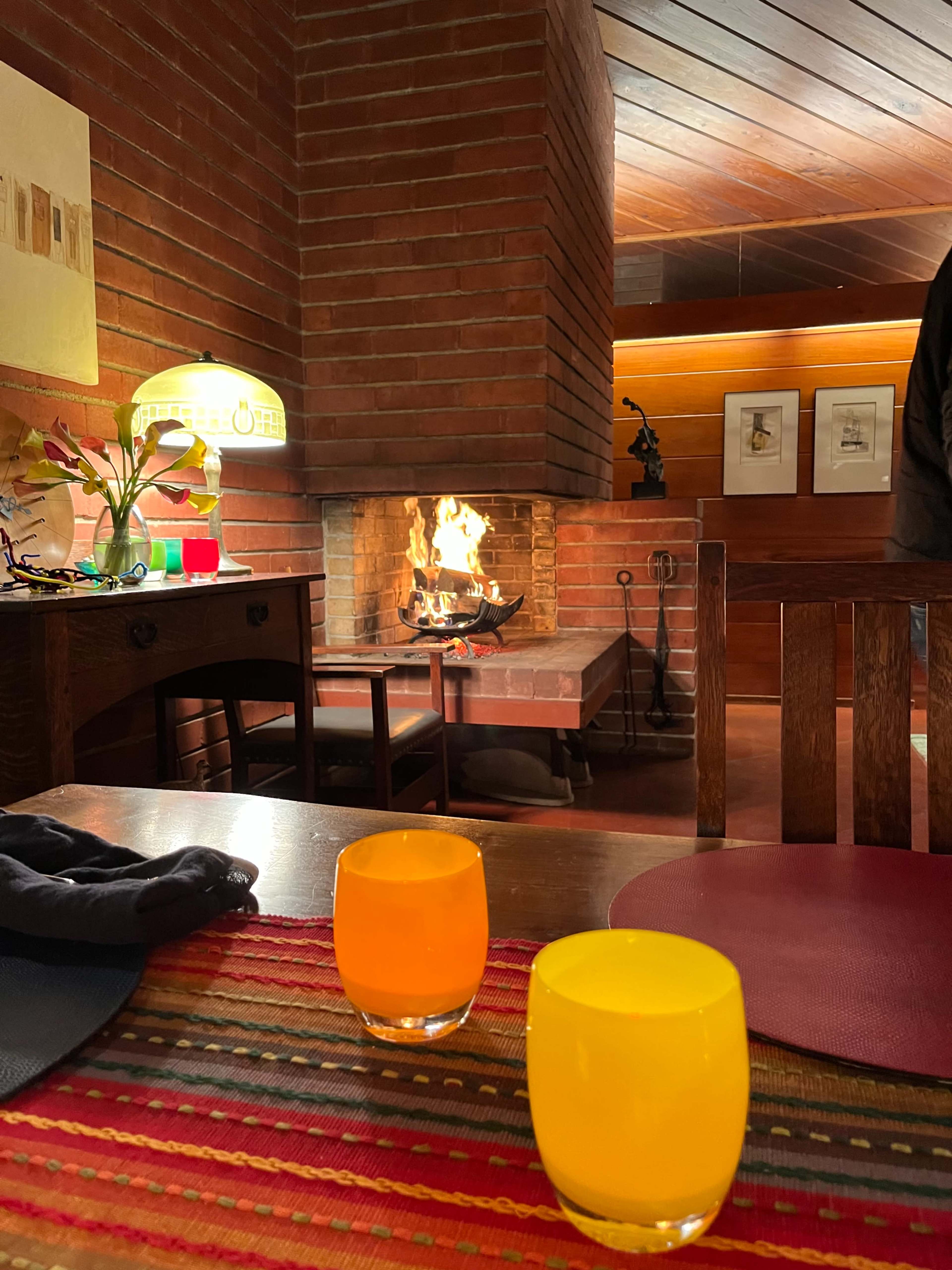 A cozy room features a fireplace with a flame, complemented by two colorful beverages in foreground glasses on a patterned table.