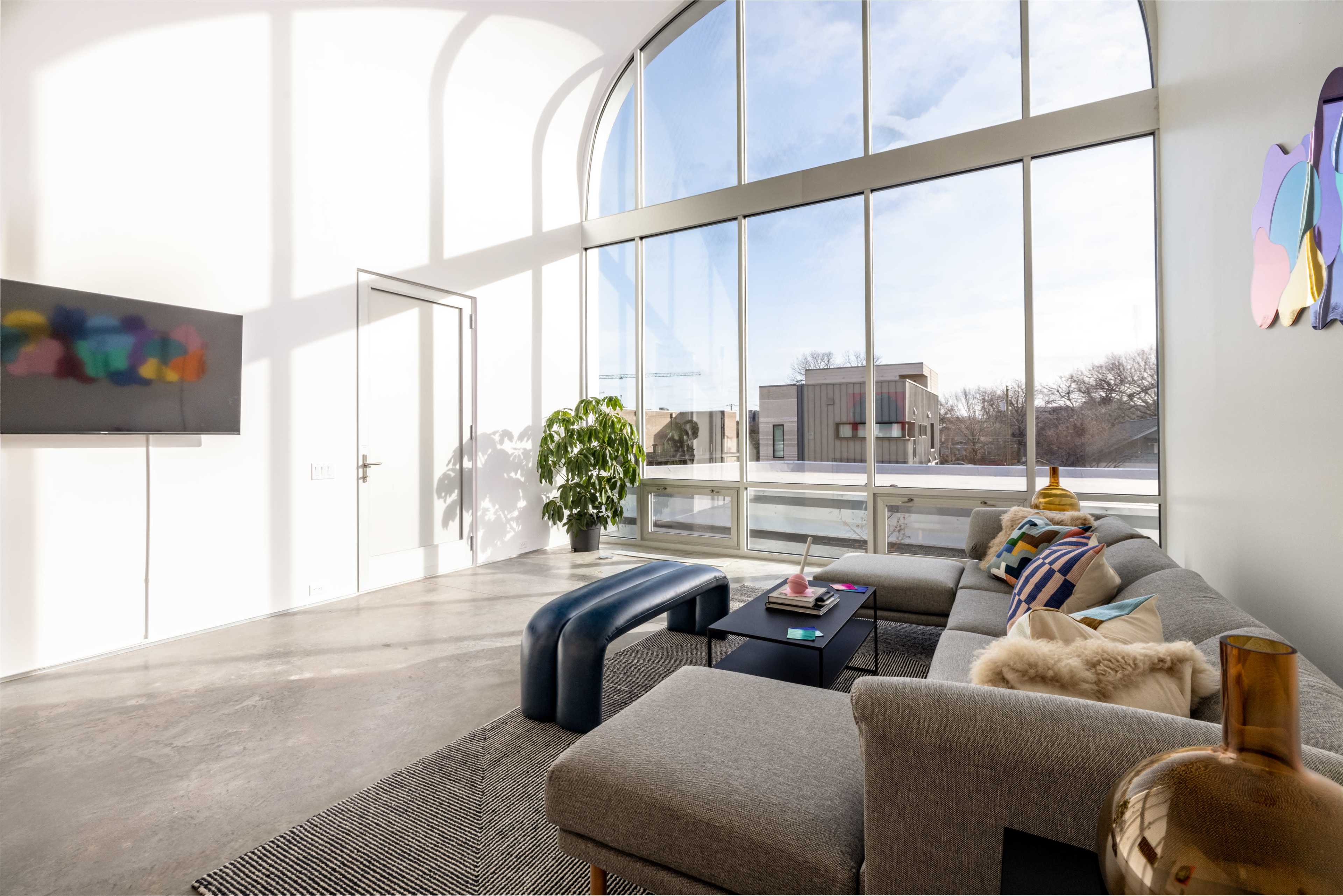A bright living room features large windows, modern furniture, and a green plant near a gray sofa.