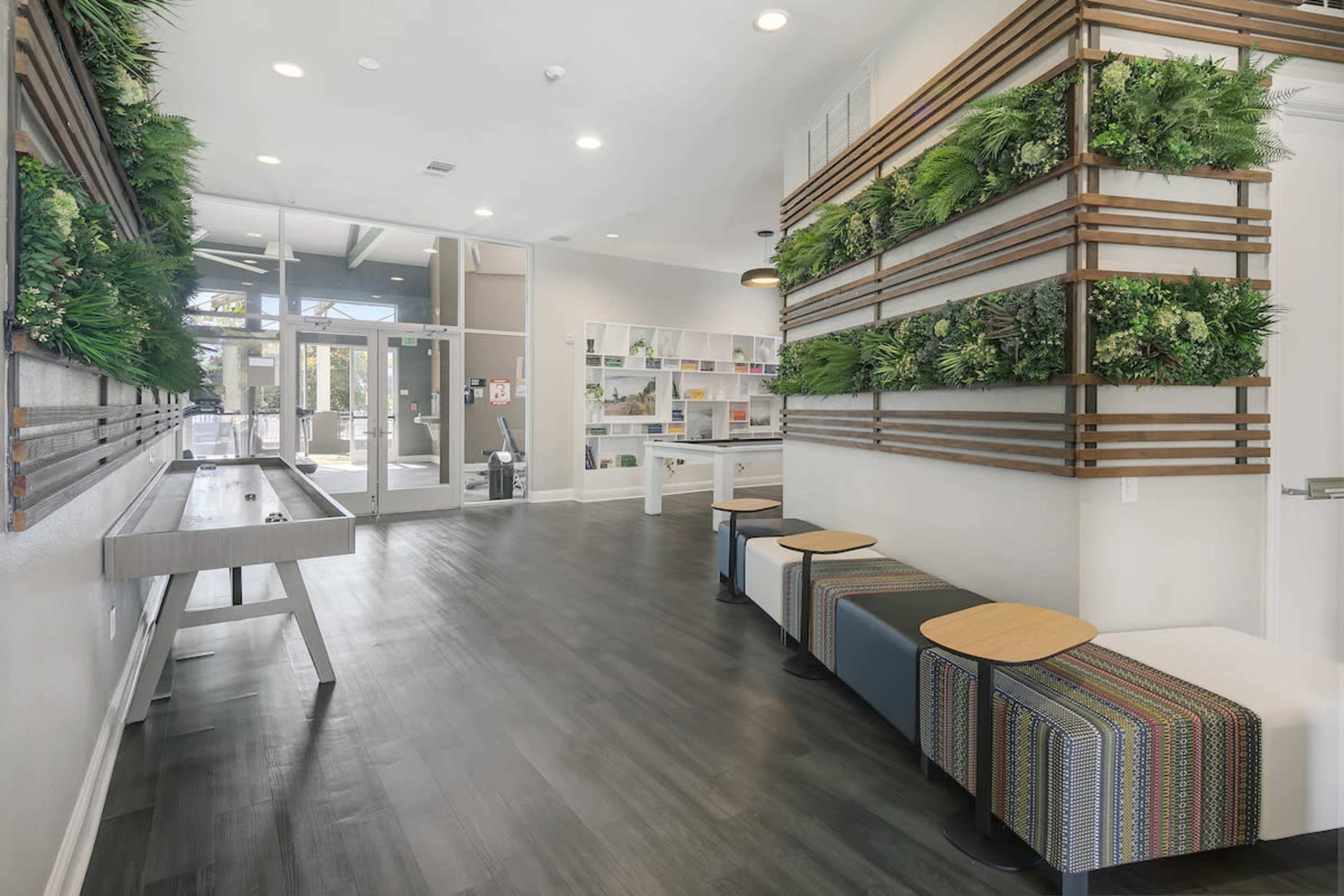A modern interior space featuring a reception area with green wall decor, benches, and seating alongside a large glass entryway.