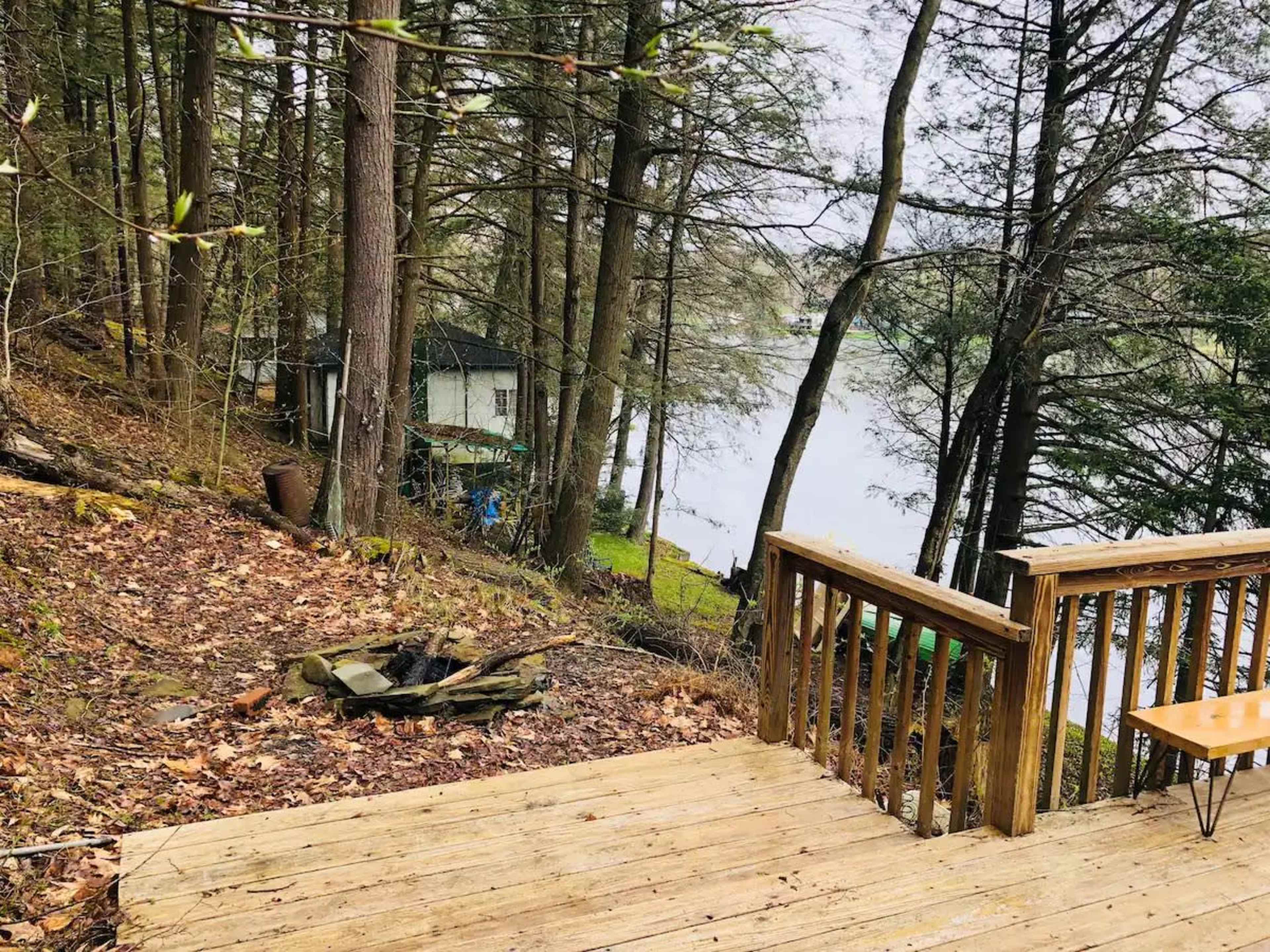 A wooden deck overlooks a grassy area leading to a calm lake, surrounded by tall trees.