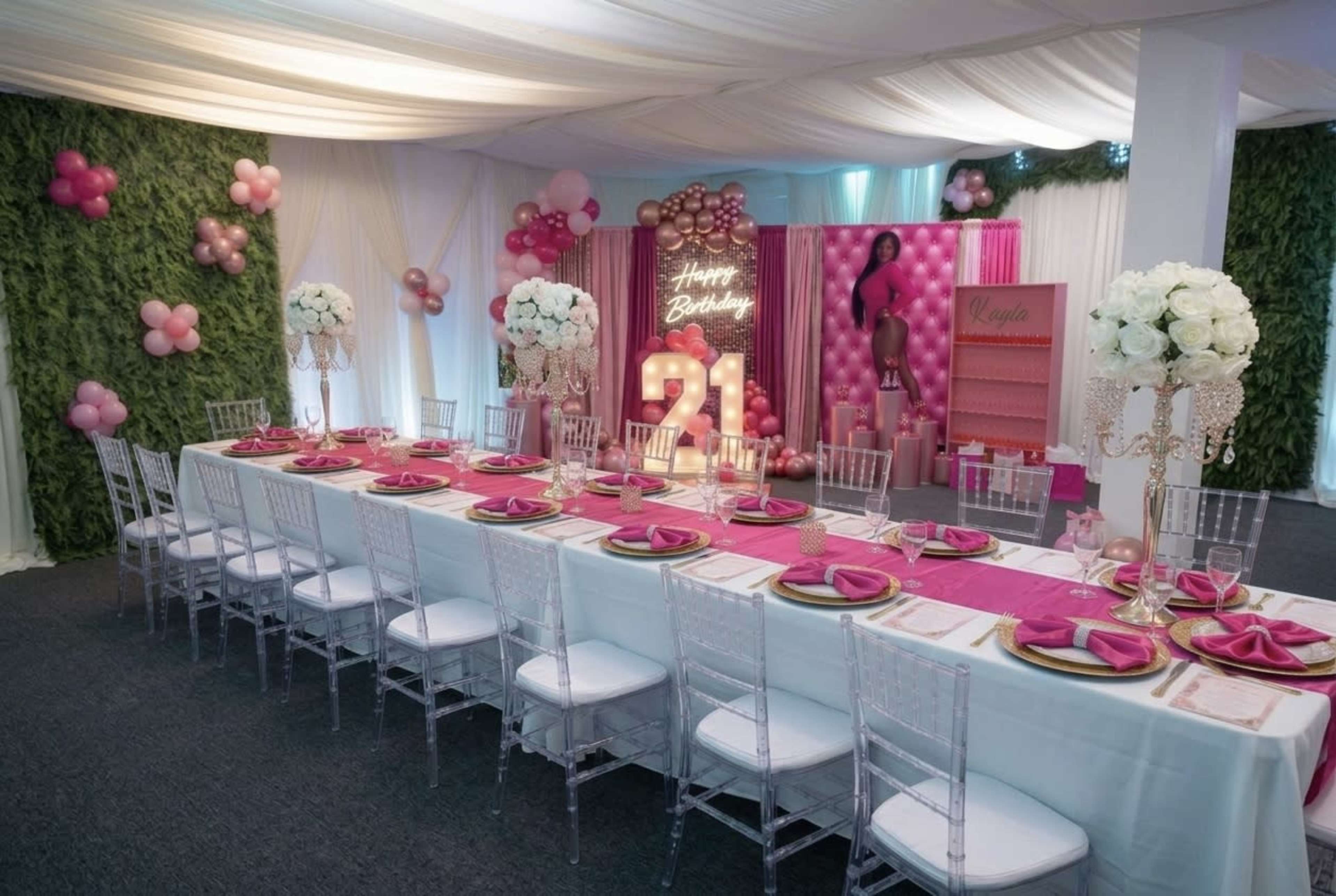 The image shows a decorated birthday party setup with a long dining table set for 21 guests, featuring pink and gold accents, floral arrangements, and a backdrop celebrating a 21st birthday.