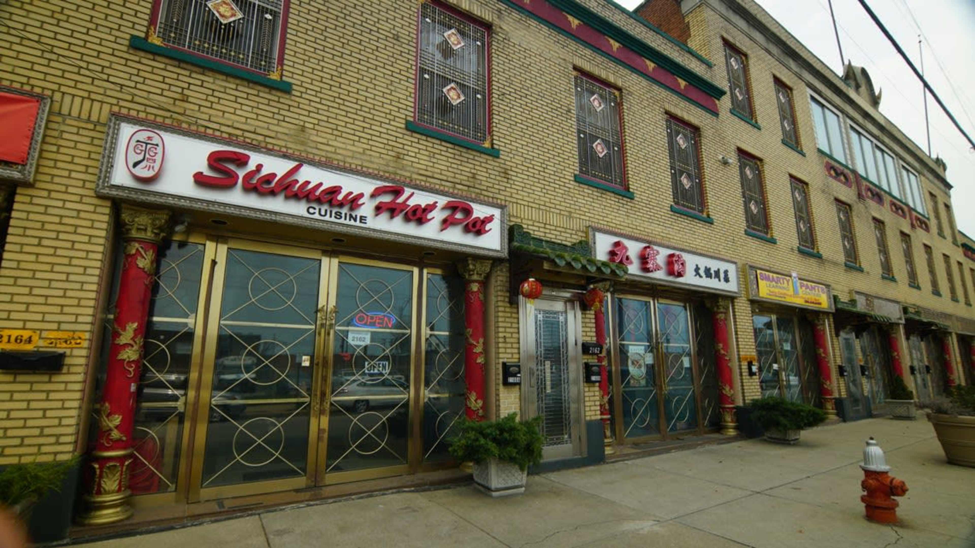 The exterior of a restaurant called "Sichuan Hot Pot Cuisine," featuring decorative elements and an adjacent building with multiple storefronts.