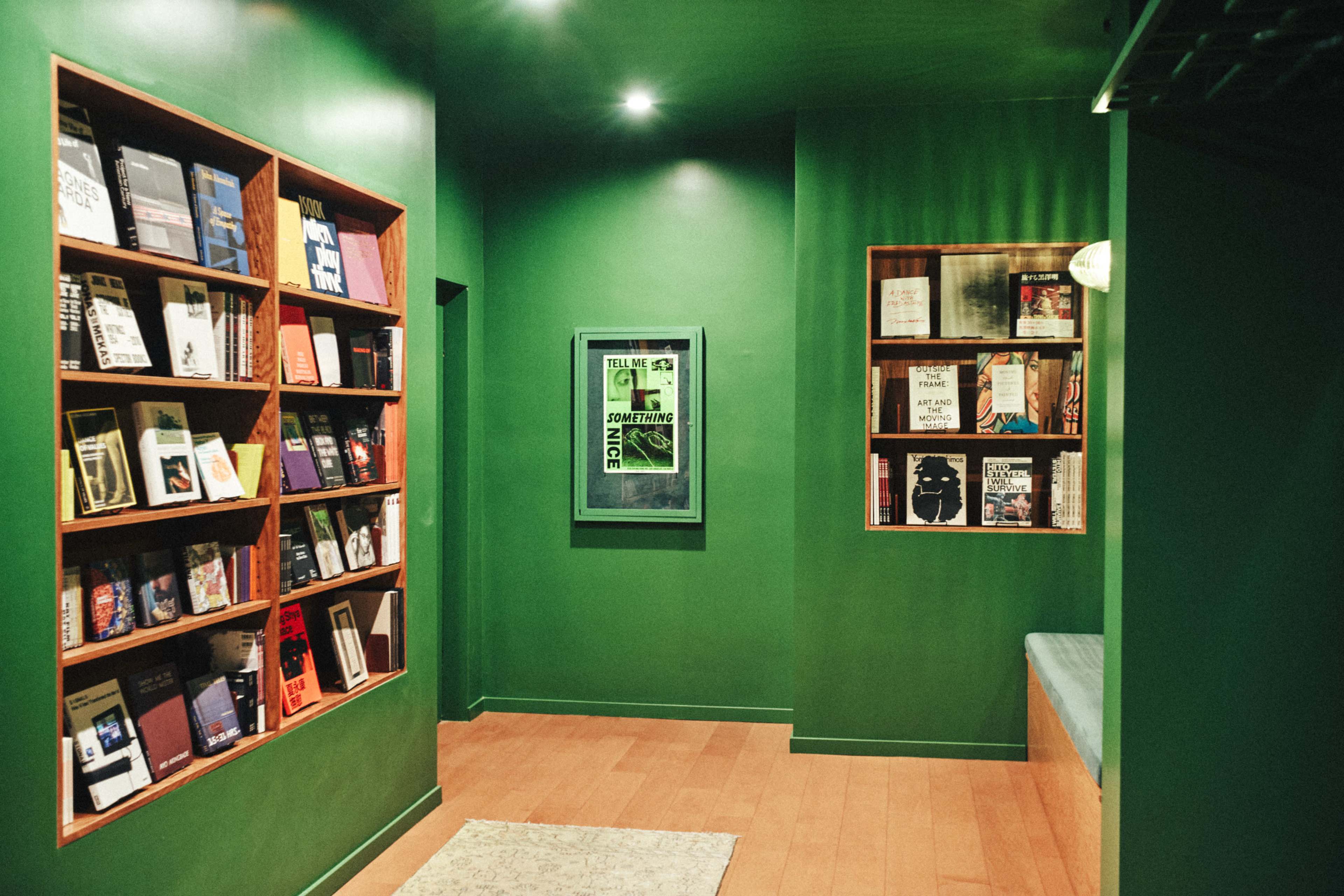 The image shows a room with green walls featuring shelves filled with books and a framed poster on one wall.