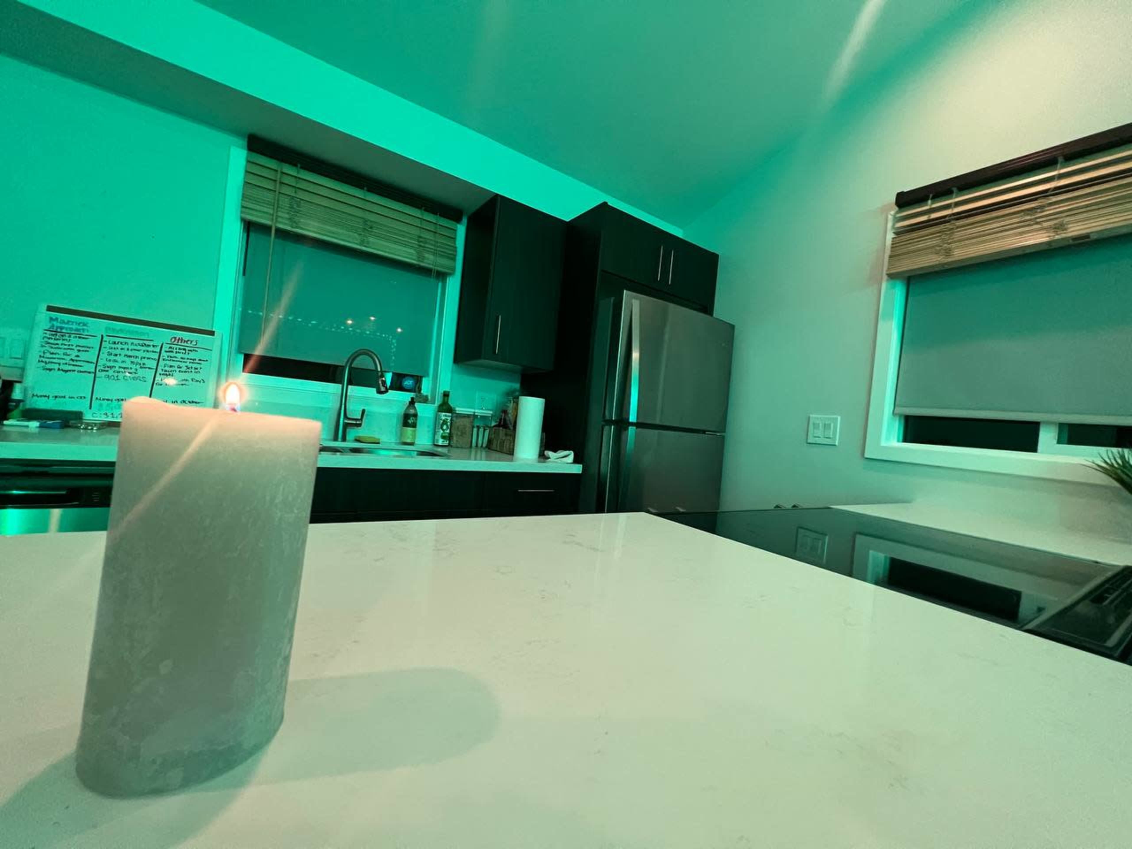 A lit candle sits on a white countertop in a modern kitchen with green lighting.