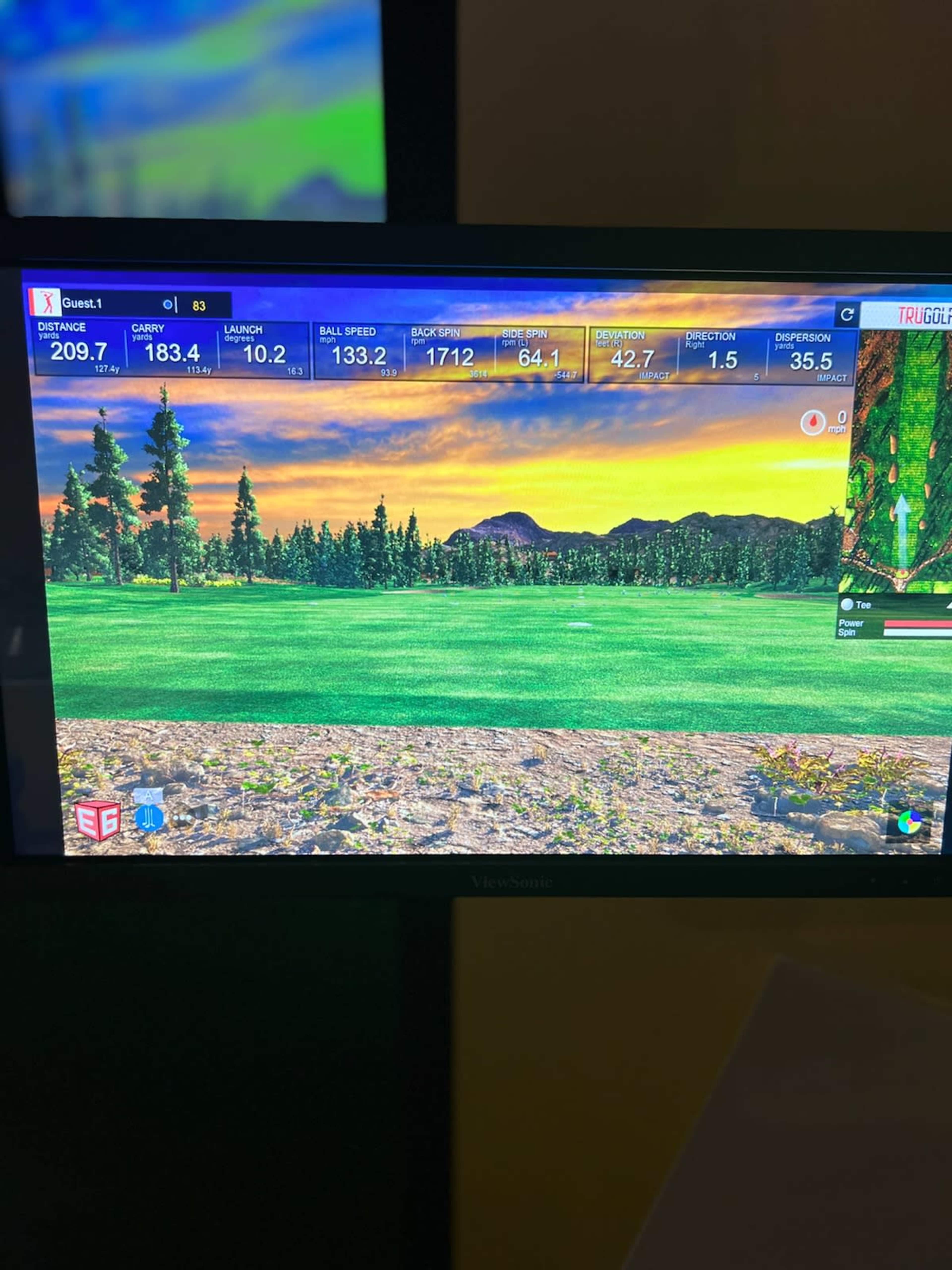 A digital golf simulator screen showing performance statistics such as distance, launch angle, ball speed, and environmental graphics of a golf course at sunset.