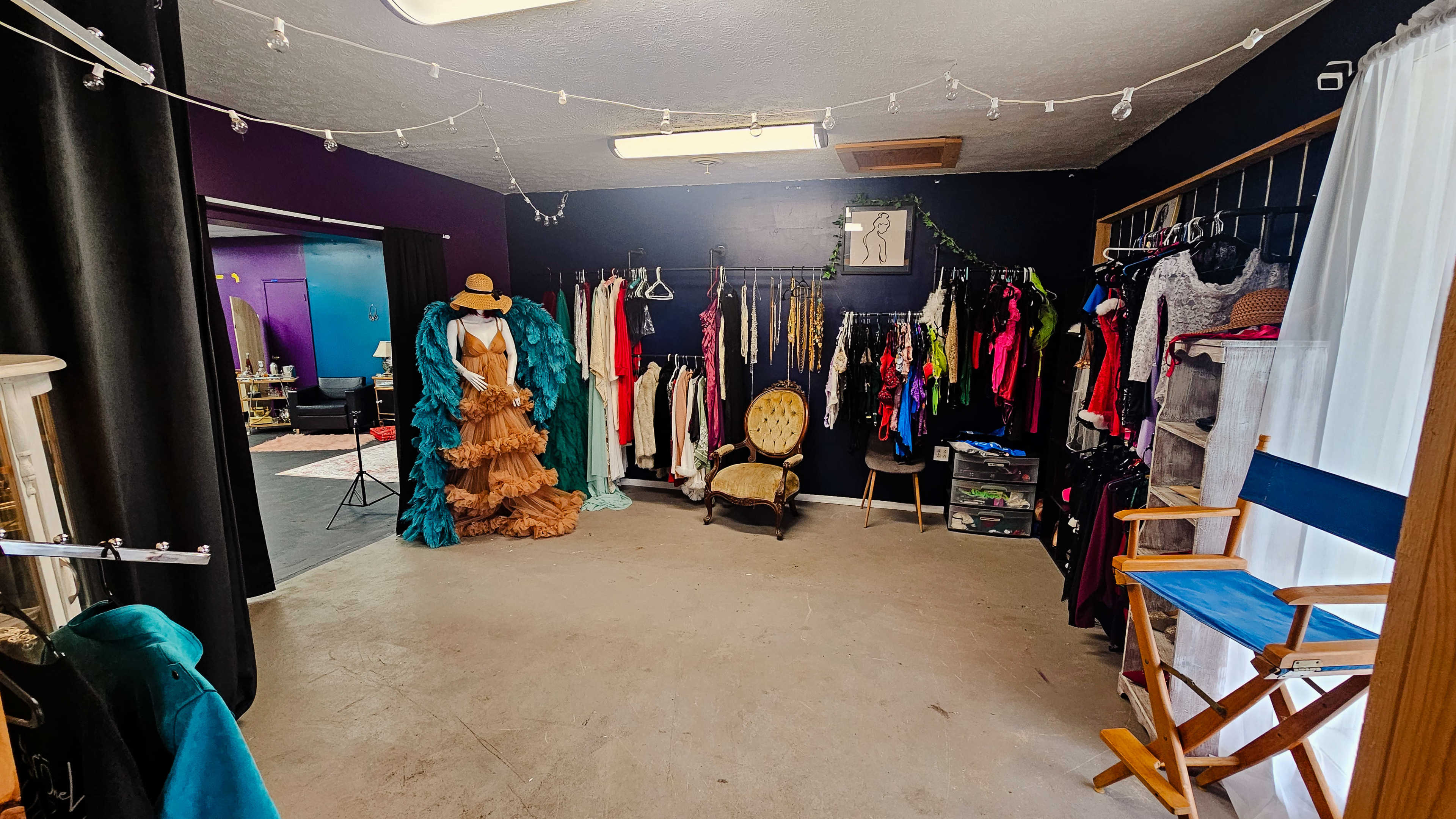 The image shows a clothing and costume rental room with various outfits hung on racks and a chair positioned in the center of the space.