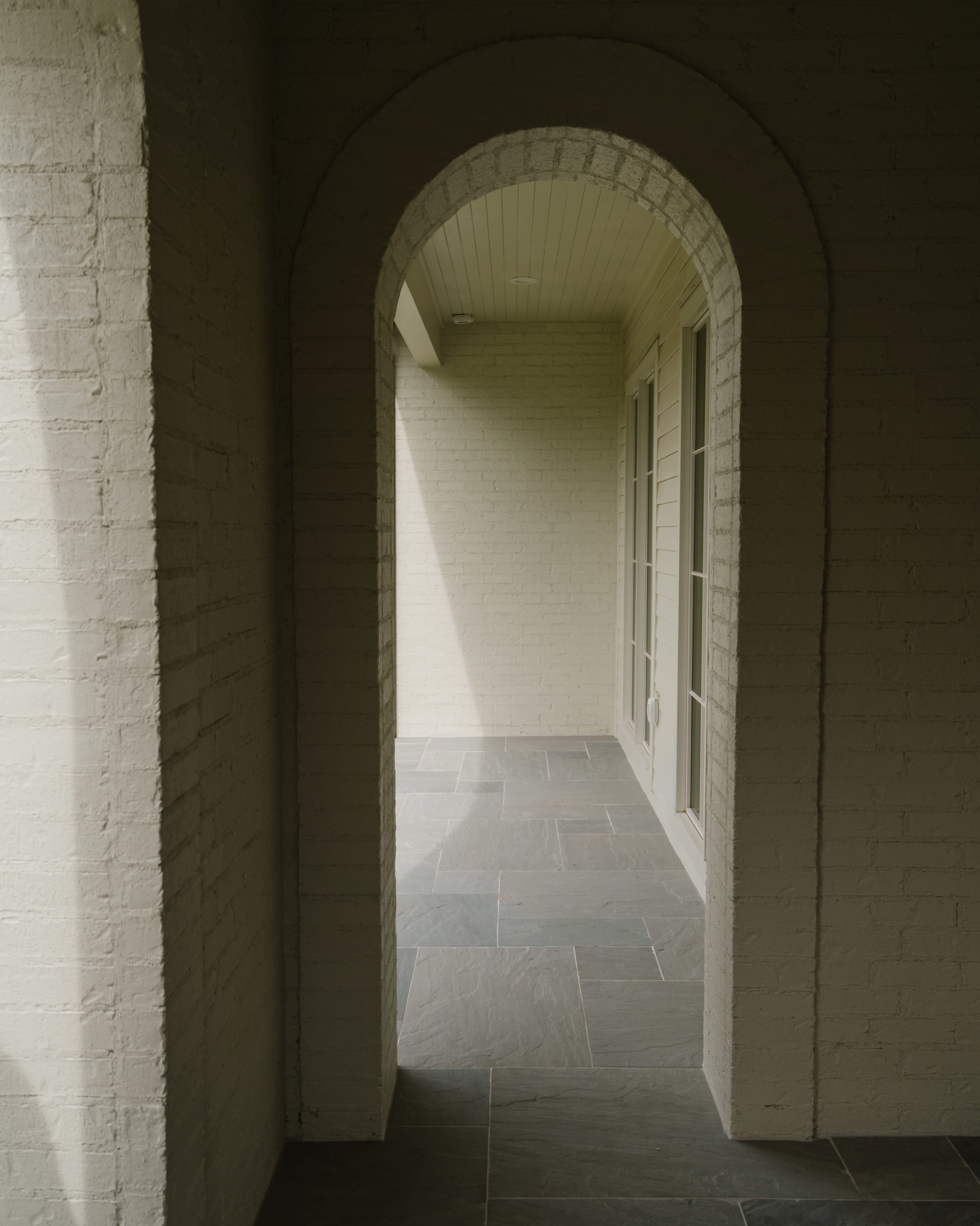 The image shows an arched doorway leading to a smooth, stone-floored corridor illuminated by natural light.