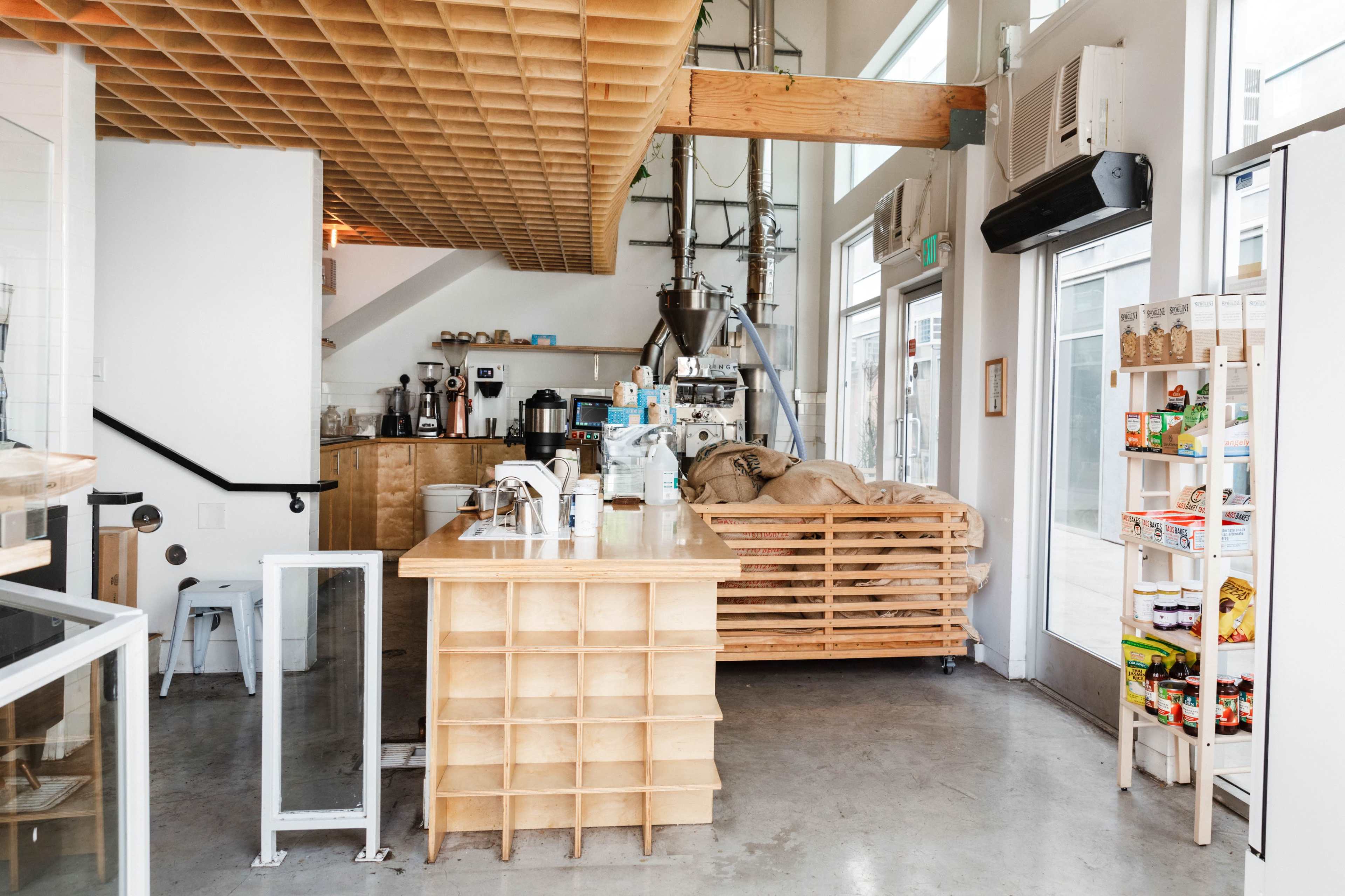 The image shows a modern cafe interior with a wooden counter, a coffee brewing area, and shelves displaying various products.
