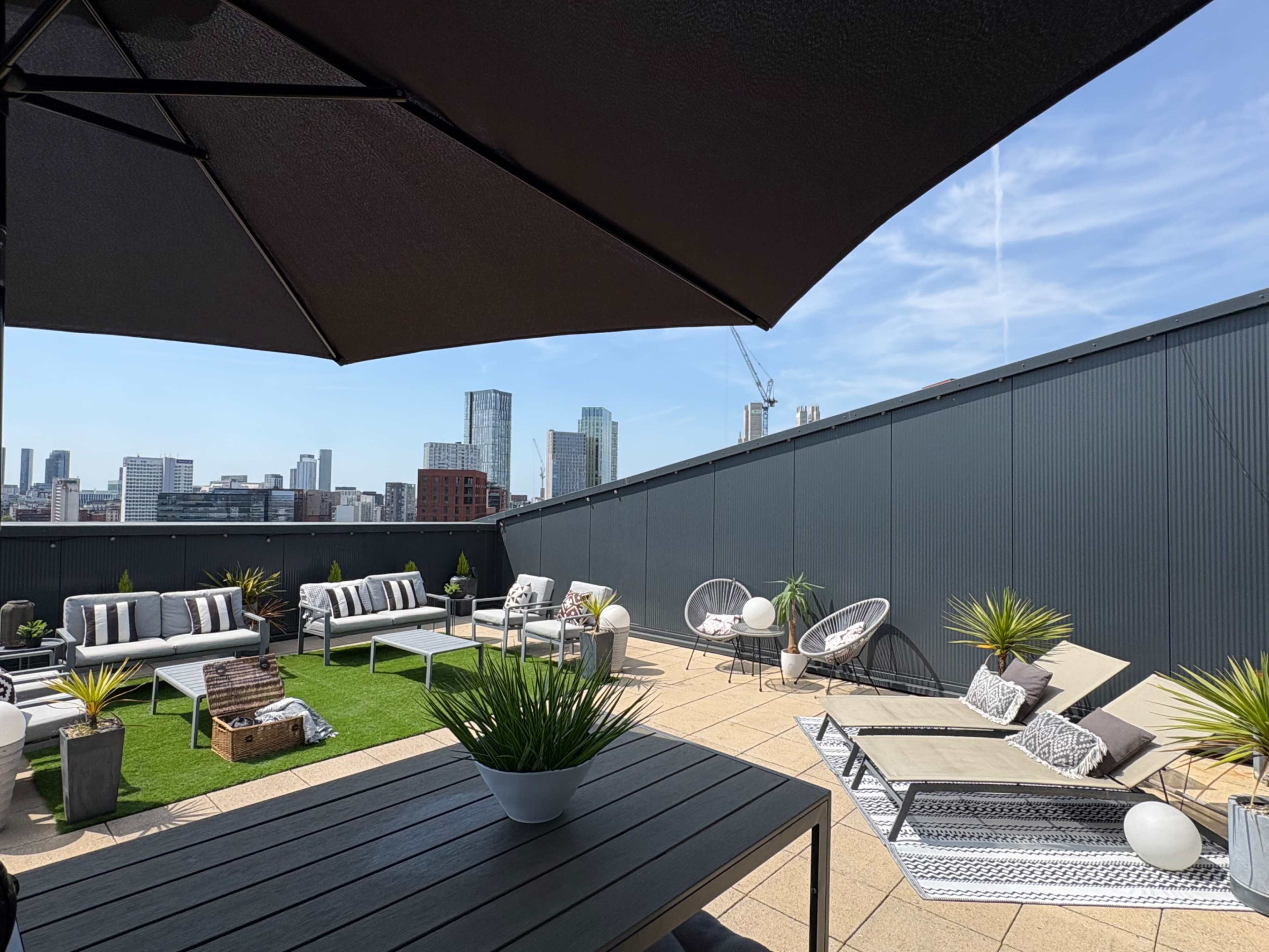 A rooftop space features lounge chairs, tables, and decorative plants, with a city skyline in the background.