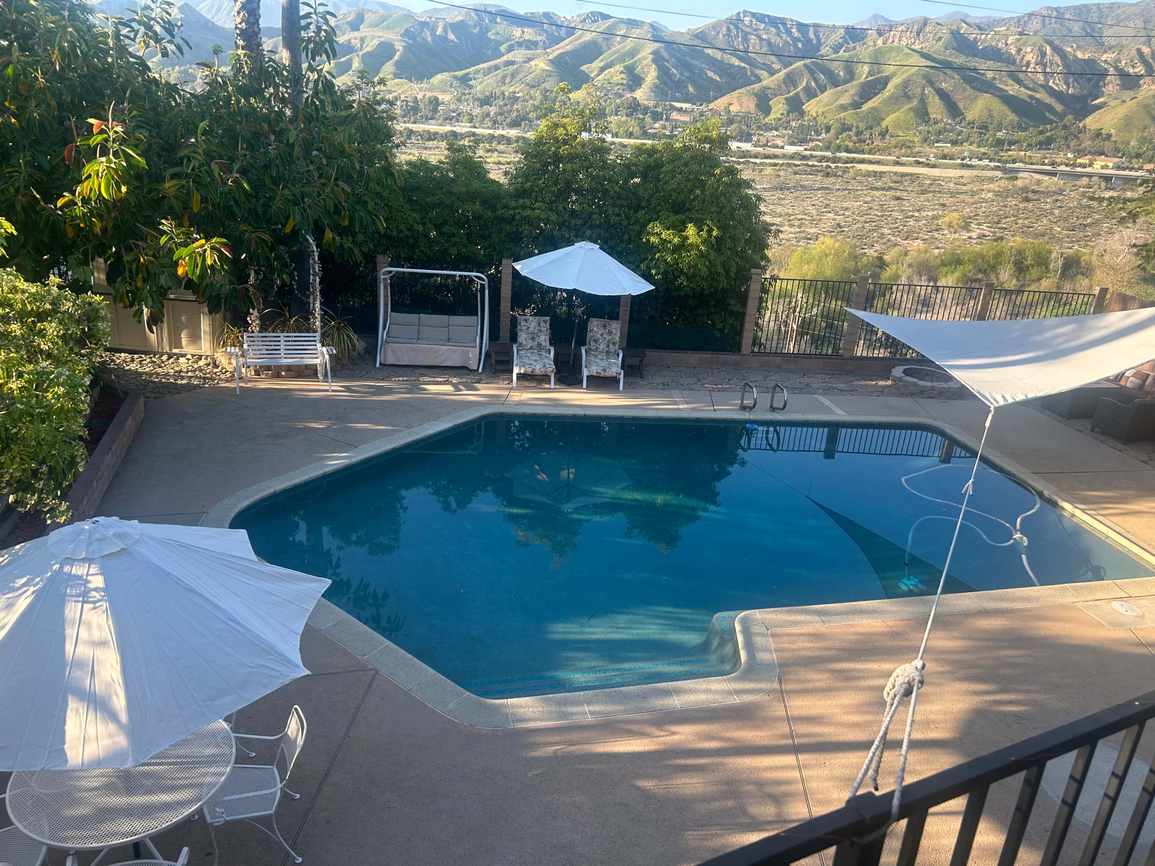 A swimming pool with umbrellas and lounge chairs is situated in a backyard overlooking a mountainous landscape.