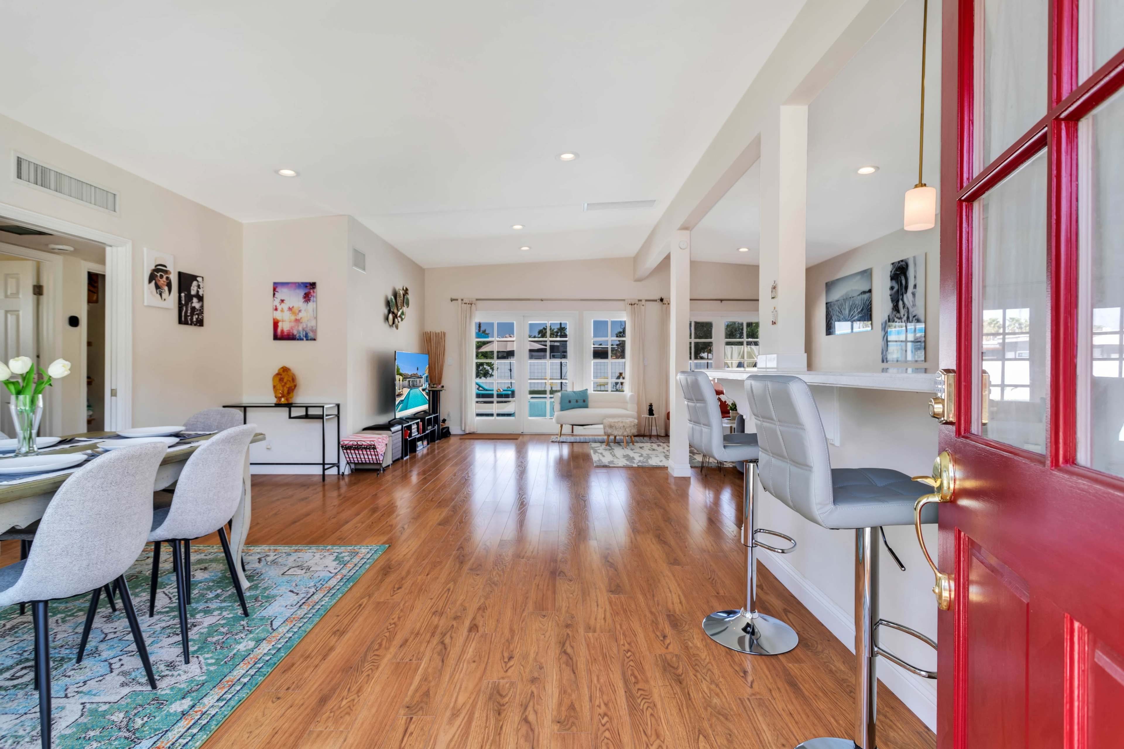 A spacious, well-lit living area with a dining table, bar seating, large windows, and wooden flooring.