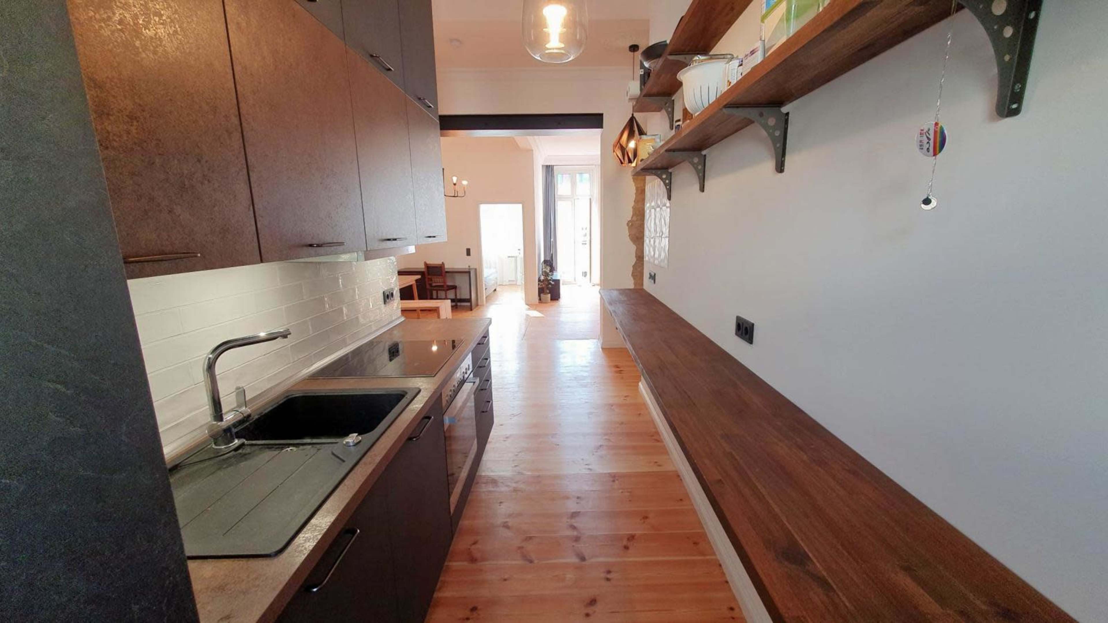 The image shows a modern kitchen with dark cabinets, a stainless steel sink, and a wooden countertop along one side.