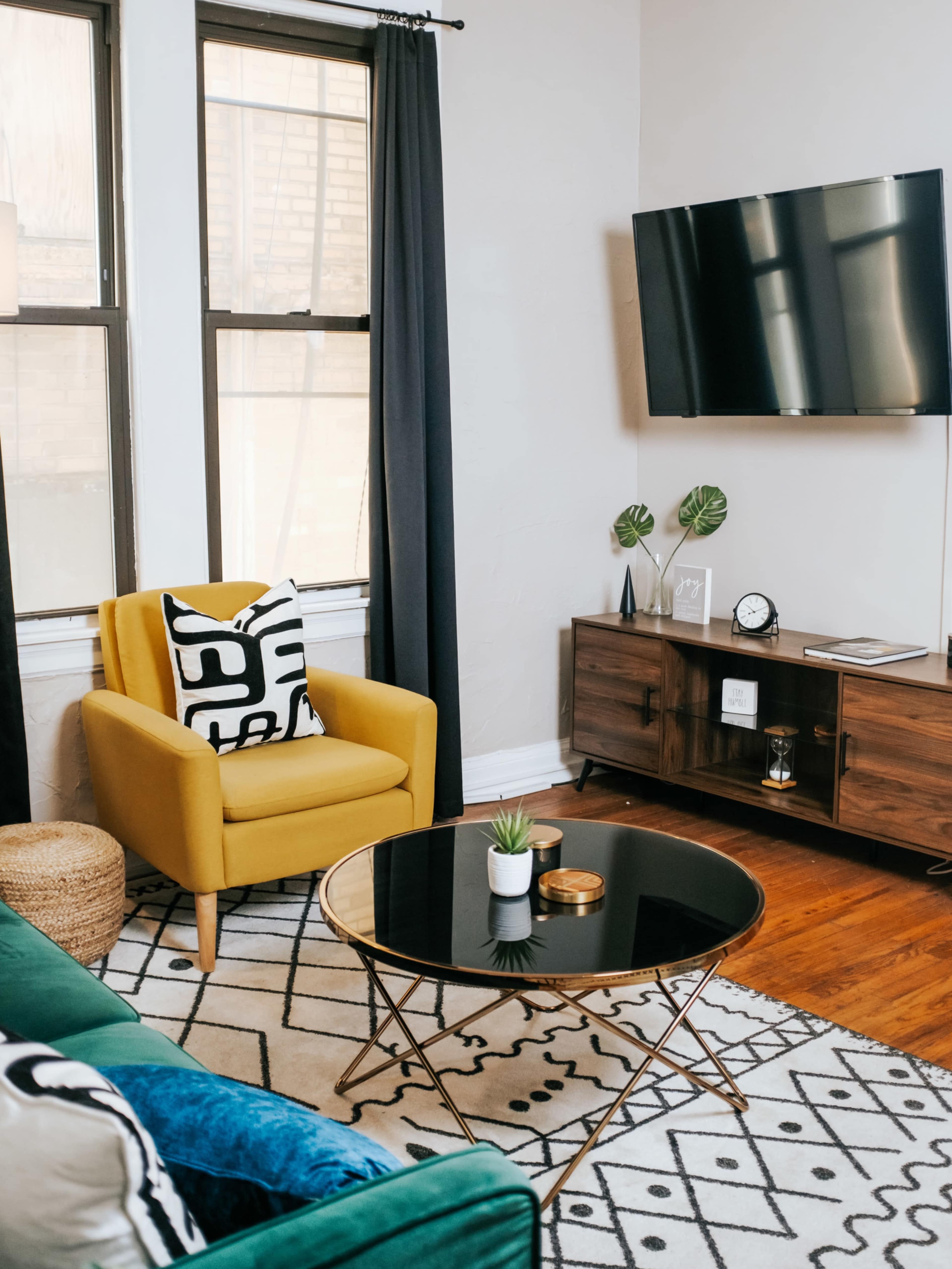 A modern living room features a yellow chair, a glass coffee table, and a wall-mounted television.