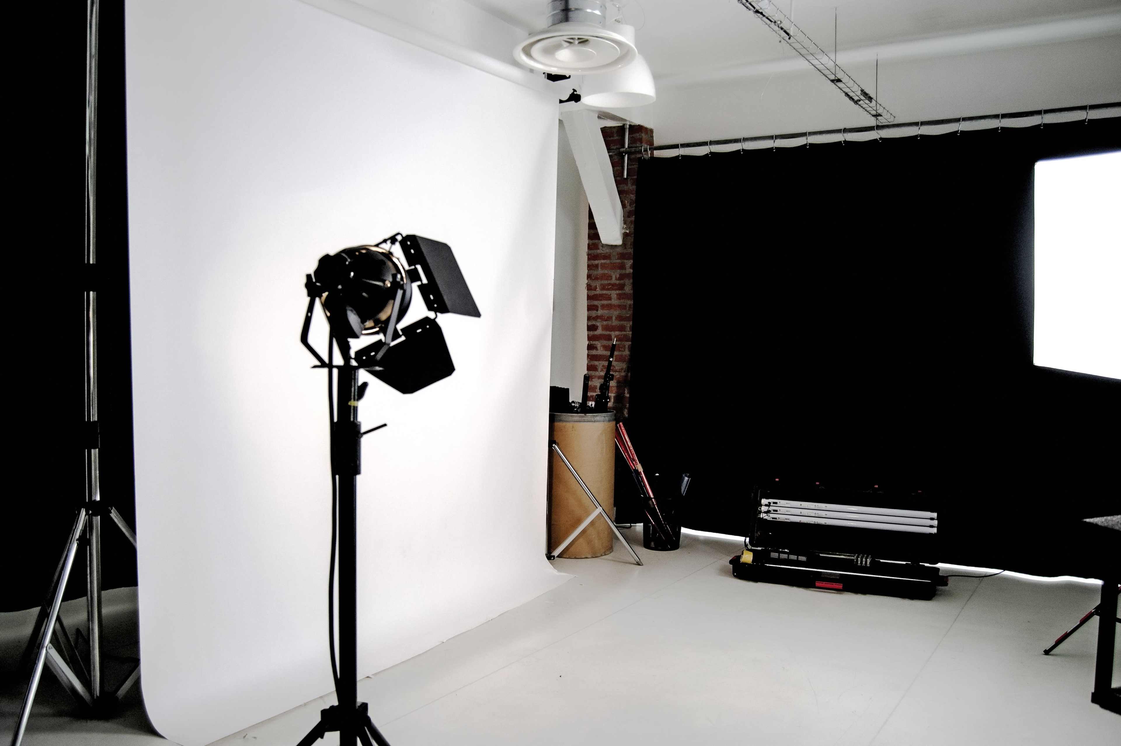 A photography studio features a white backdrop, lighting equipment, and black fabric drapes.