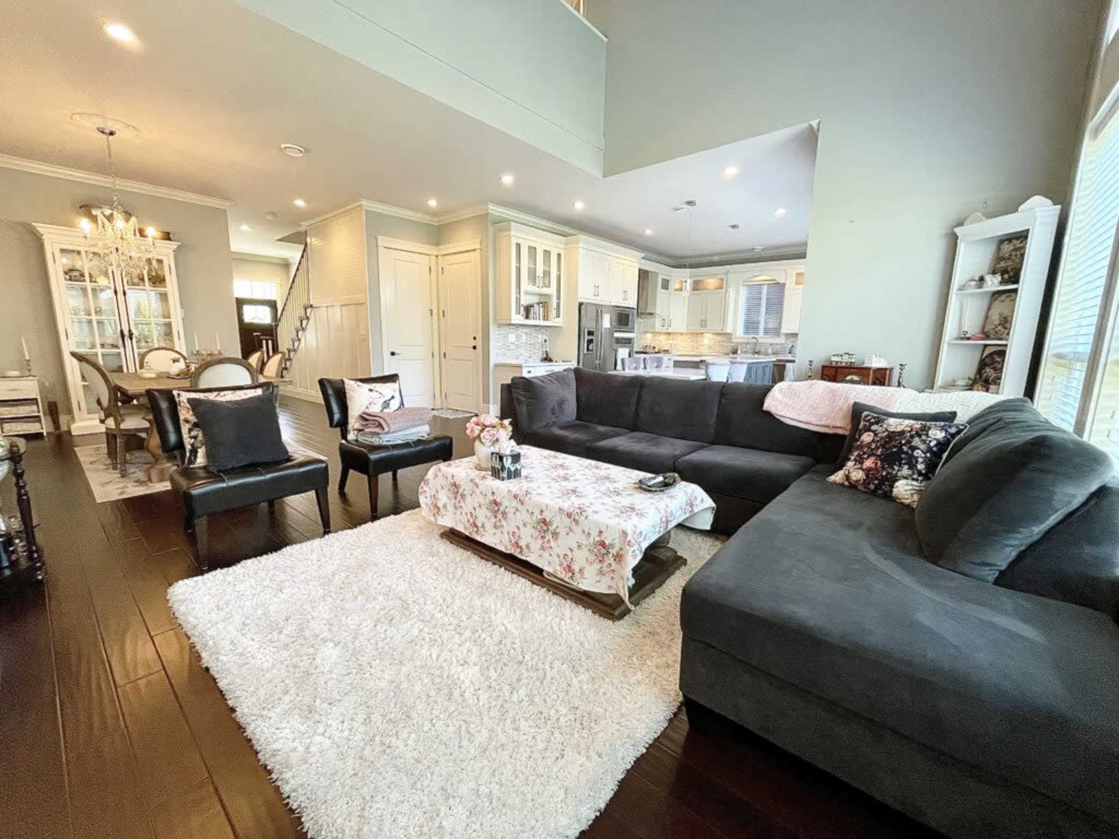A modern living room with a dark sectional sofa, a floral-patterned coffee table cover, and a dining area visible in the background.