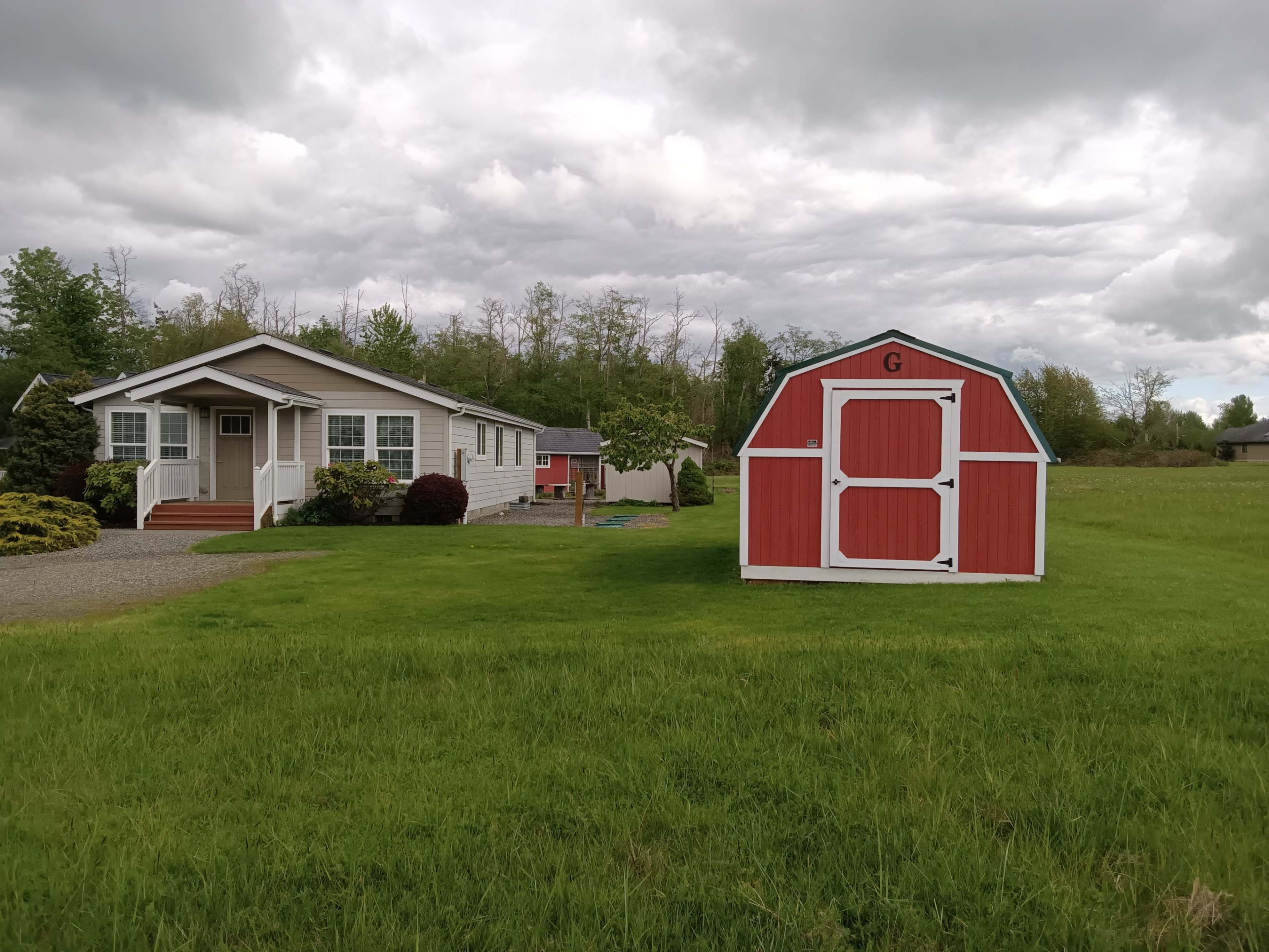 A white house with a porch sits next to a red barn in a grassy area under a cloudy sky.