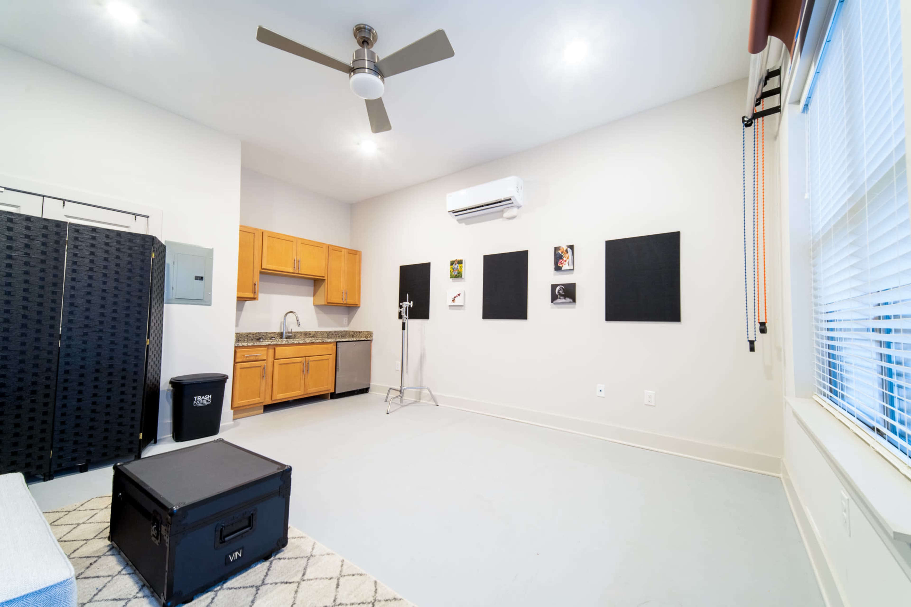 The room features a kitchenette with wooden cabinets, a black folding screen, and several framed artworks on the walls.