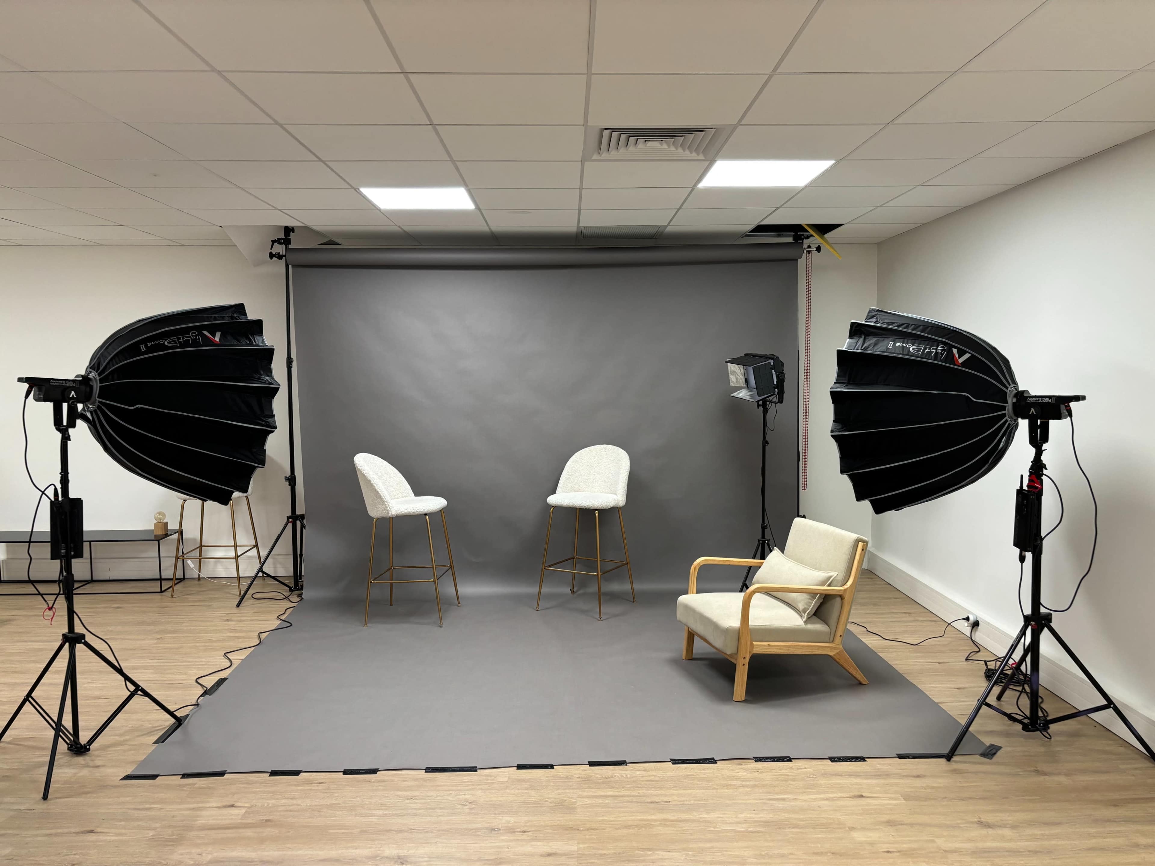 A photography studio setup with two high stools, a chair, and studio lighting on either side of a gray backdrop.