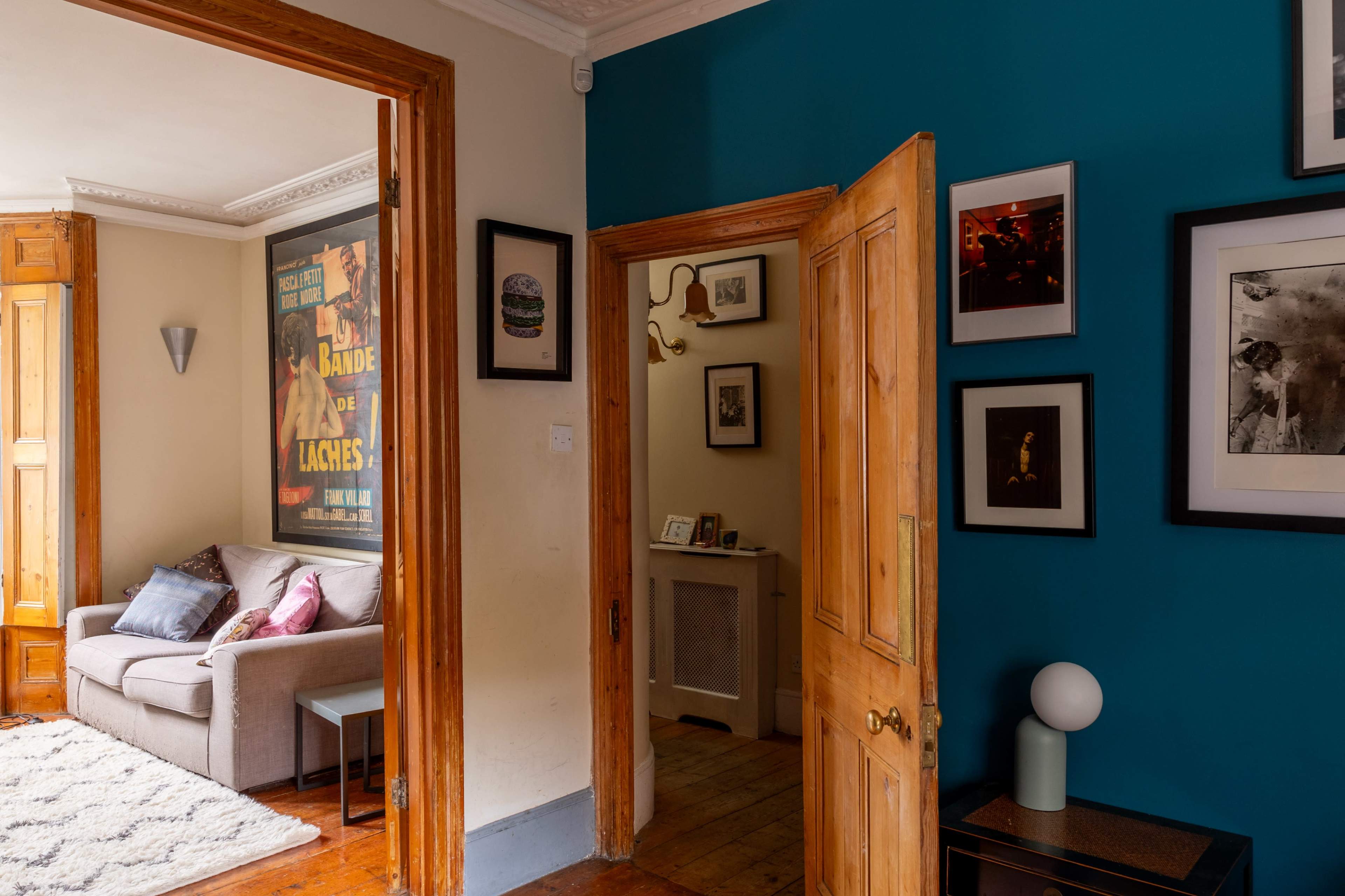 A corridor leading to a cozy living room with a gray sofa and colorful wall art, flanked by wooden doors and a blue accent wall.