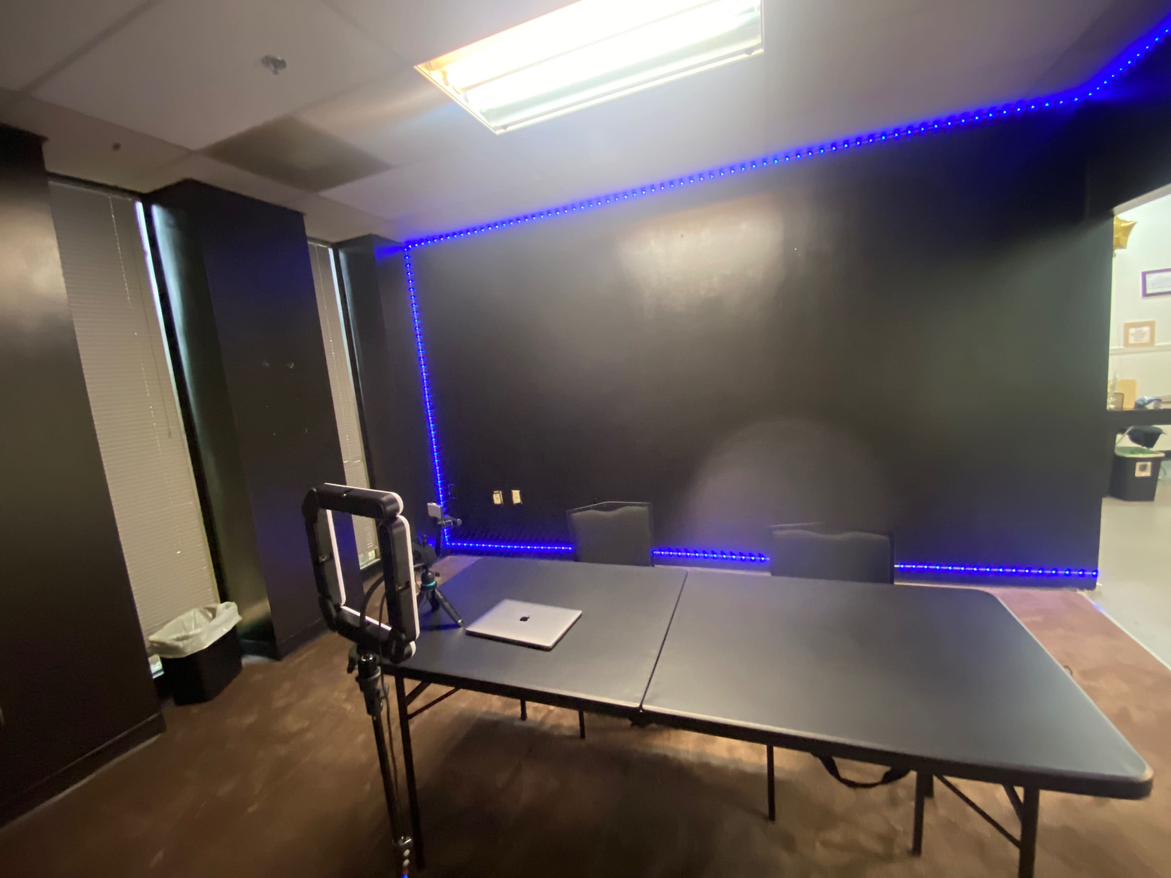 The image shows a conference room with a black wall, a long black table, two chairs, and blue LED lighting outlining the wall.