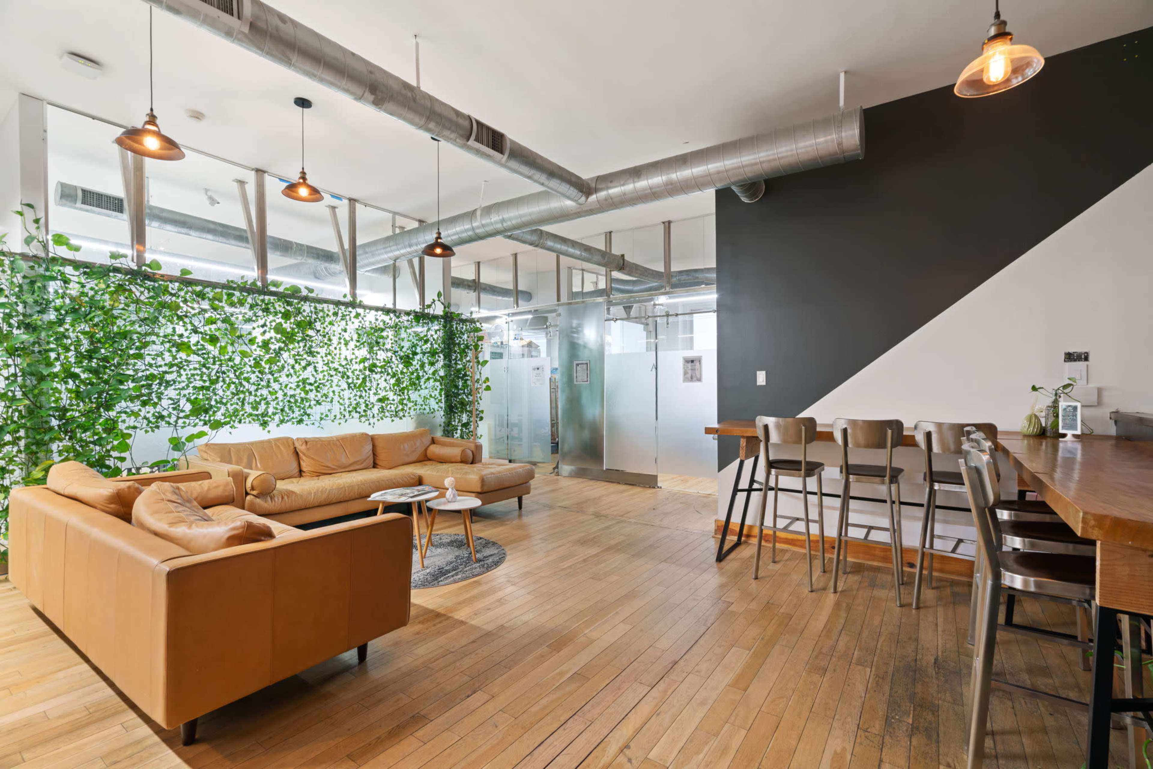 The image shows a modern, spacious living area with a tan leather sofa, a wooden dining table, and a vertical garden on one wall.
