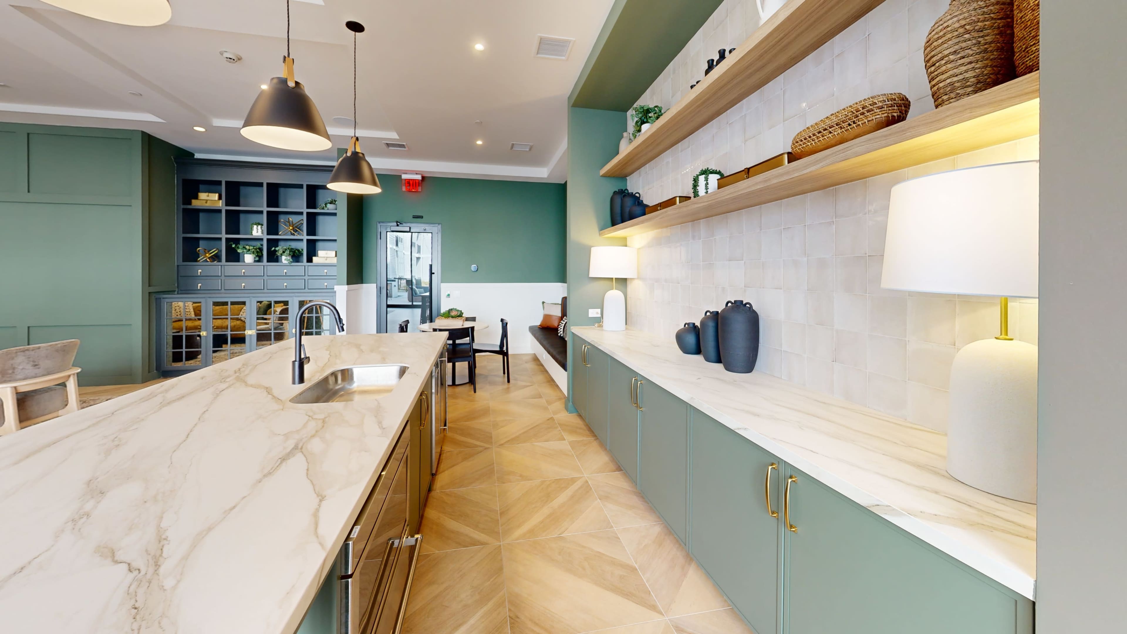 The image shows a modern kitchen with a marble countertop, green cabinetry, open shelves displaying decorative items, and ample lighting.