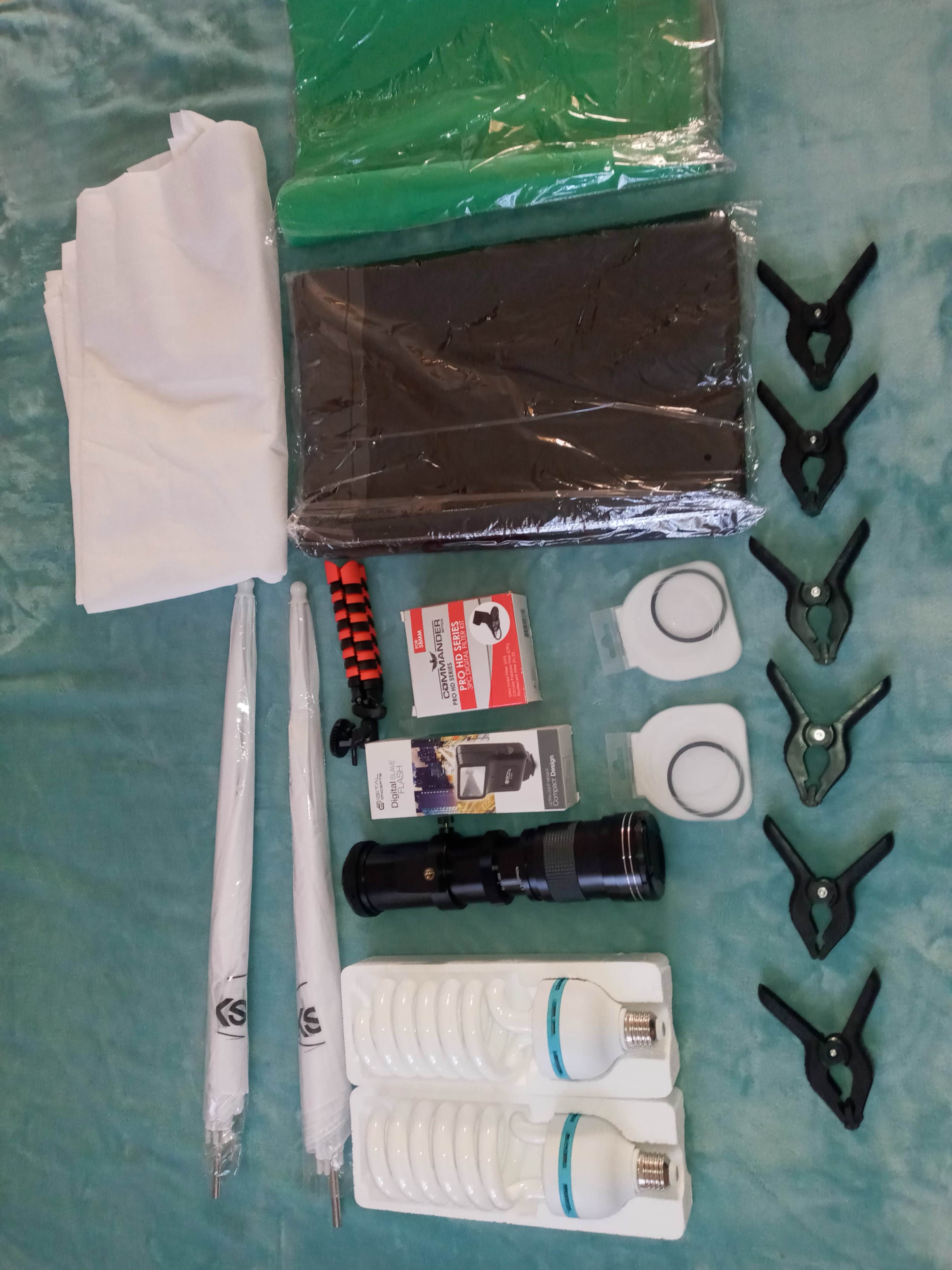 Various photography accessories arranged neatly, including backdrop rolls, clamps, light bulbs, umbrellas, and a flashlight.