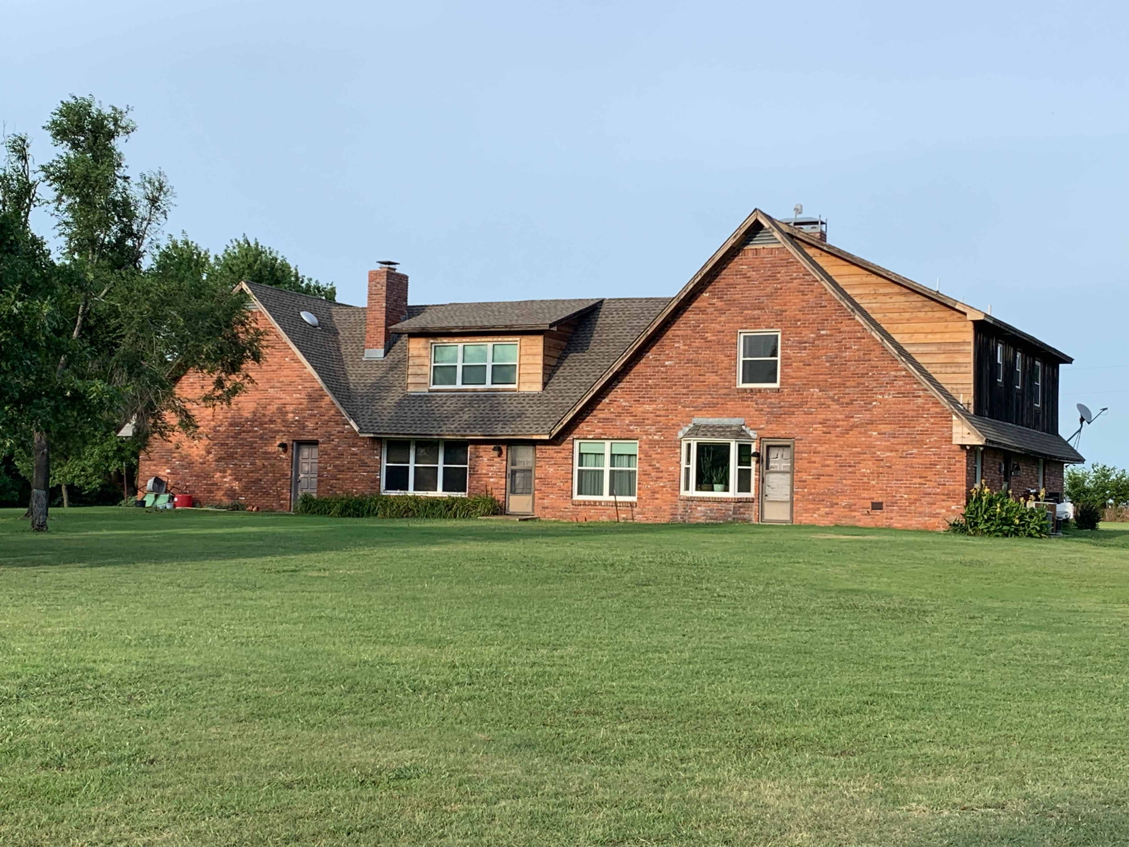 A red brick house with a sloped roof and a mix of wood siding sits on a grassy lawn.