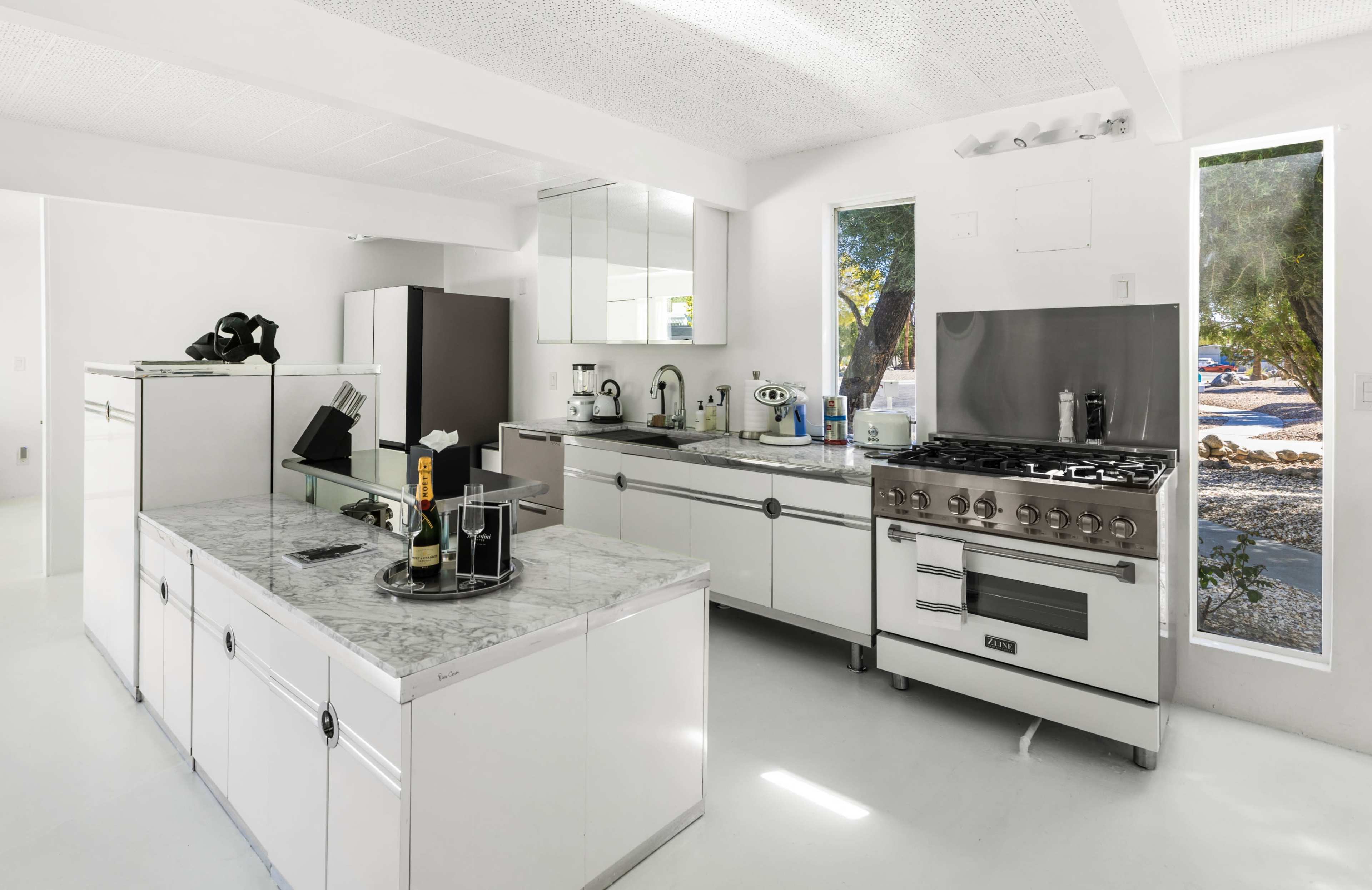 The kitchen features white cabinetry, marble countertops, and modern appliances, with large windows providing natural light.