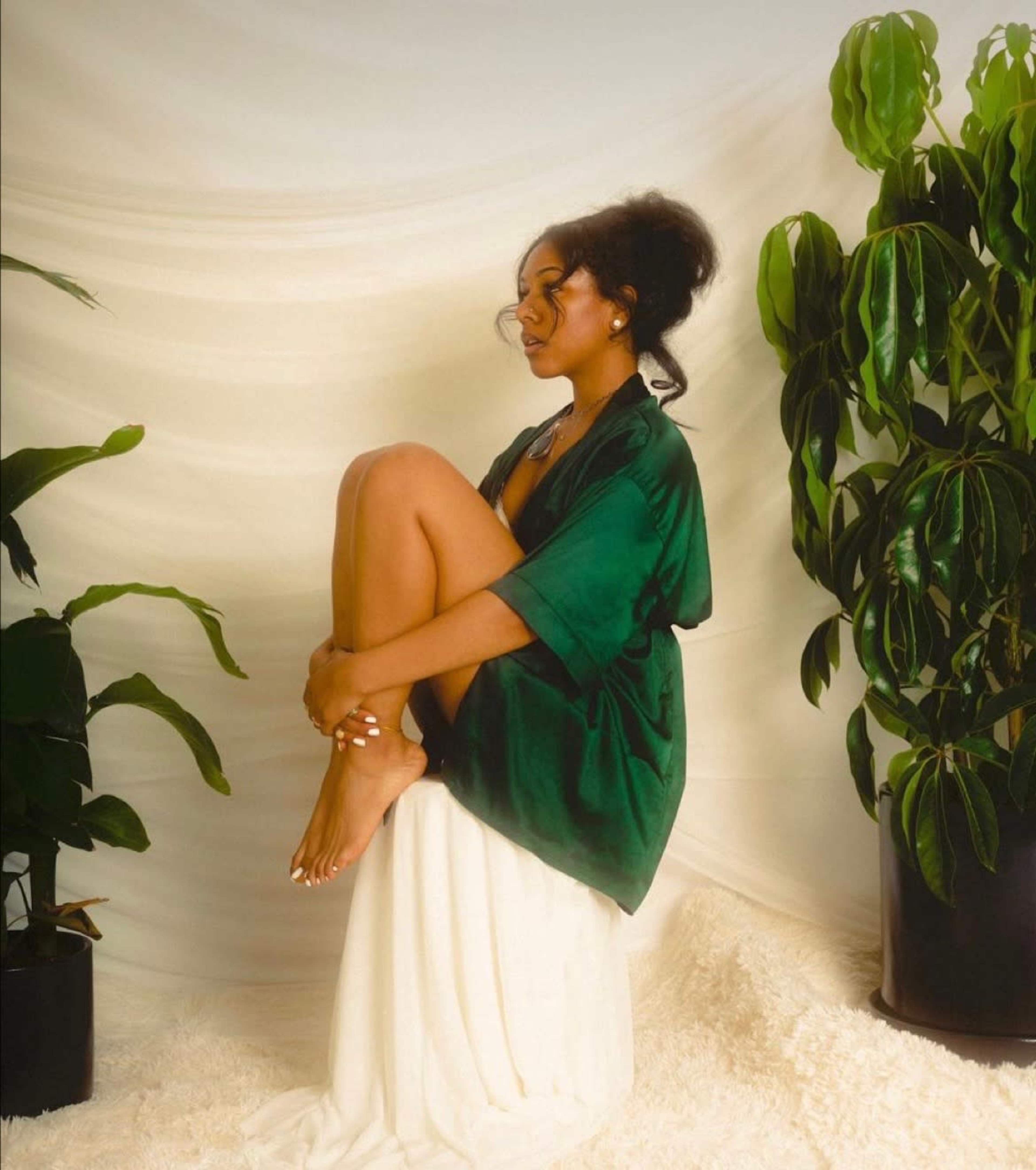A person sitting on a pedestal draped in a white cloth, surrounded by potted plants.